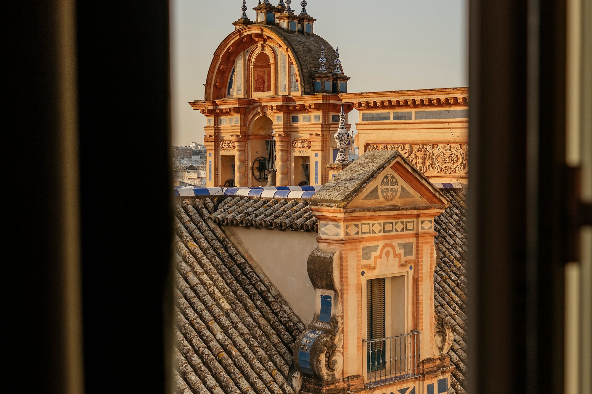 Seville rooftop view through window: ornate dome, terracotta tiled roofs.