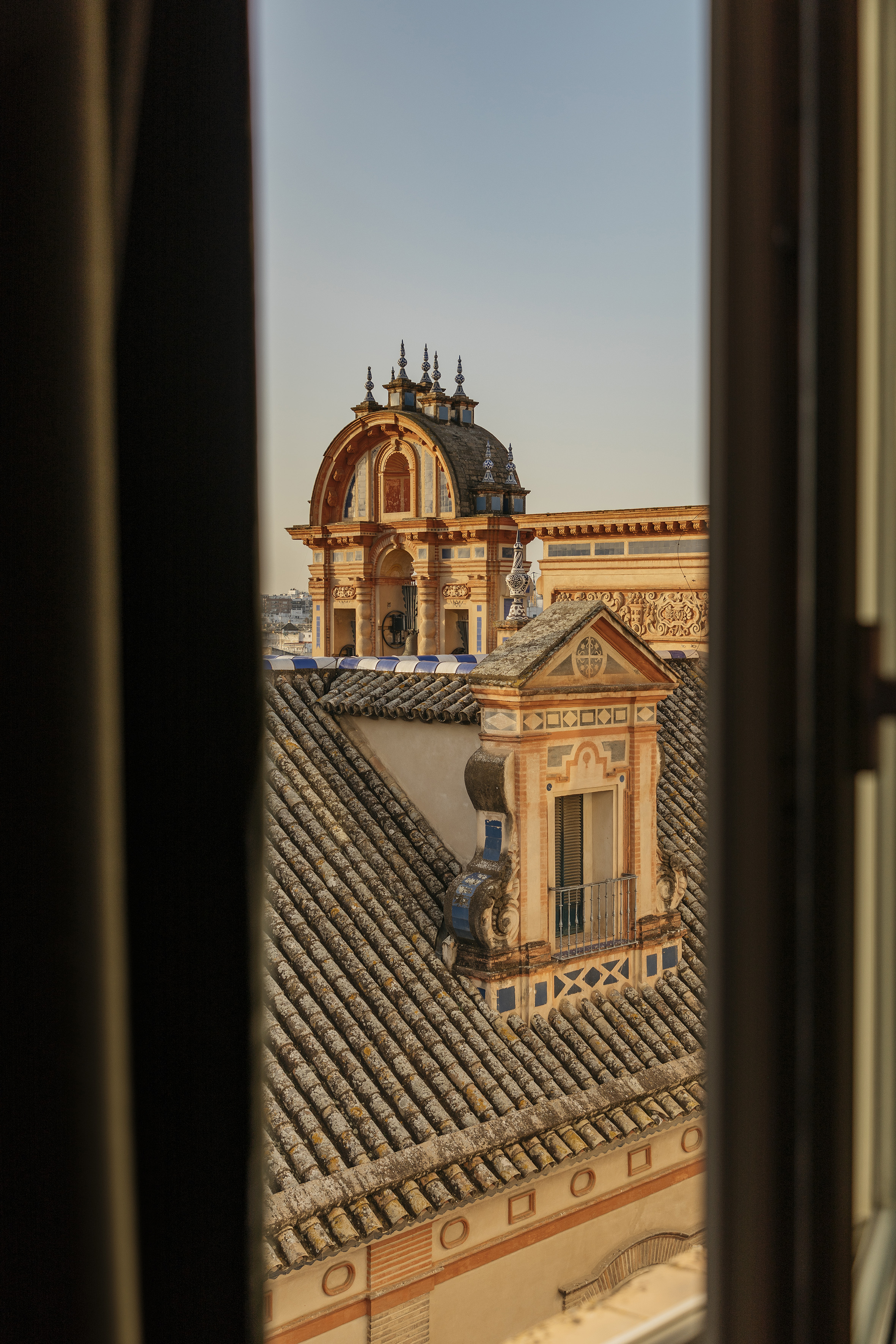 Seville rooftop view through window: ornate dome, terracotta tiled roofs.