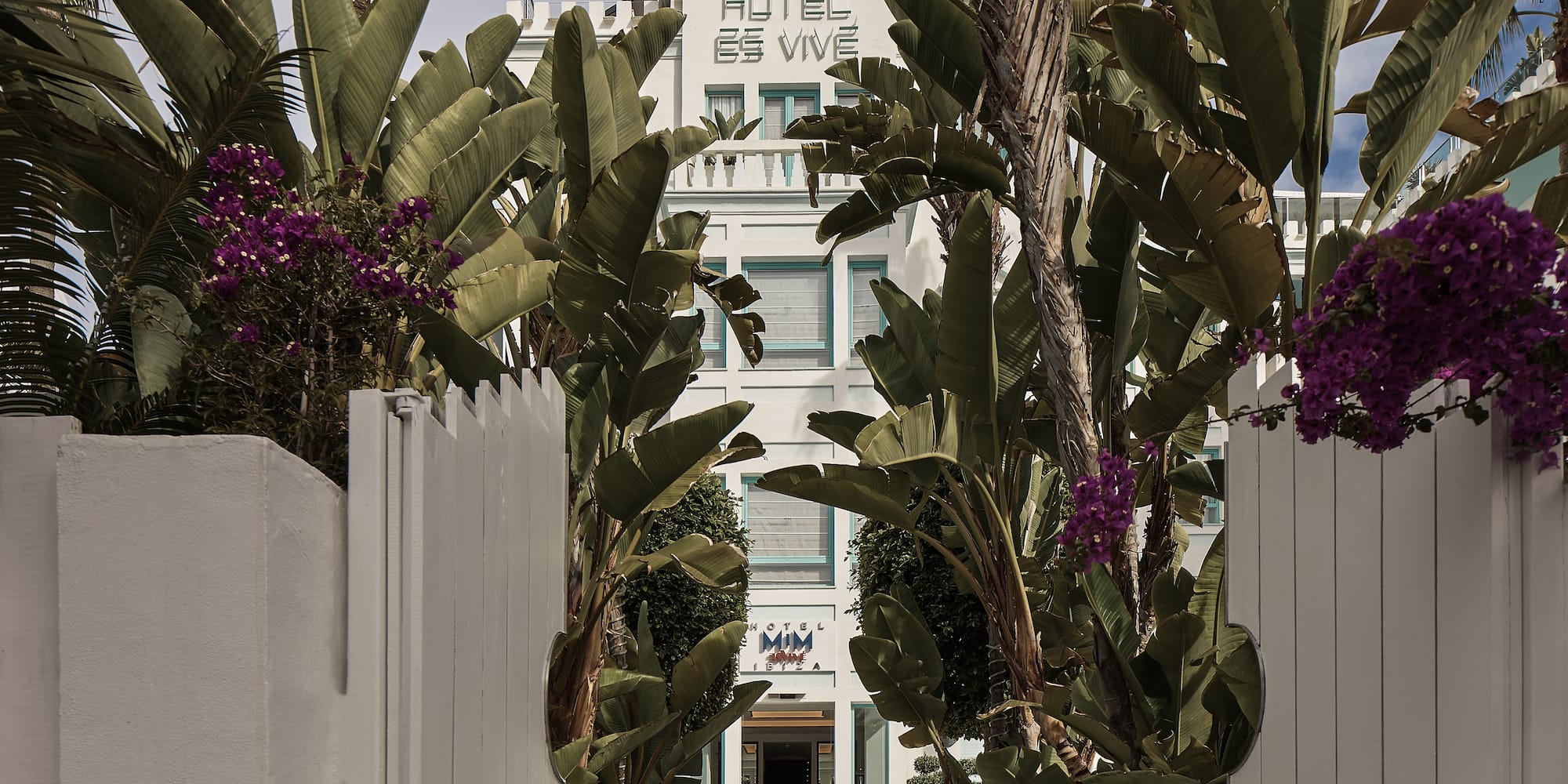 a white building with palm trees and a white fence