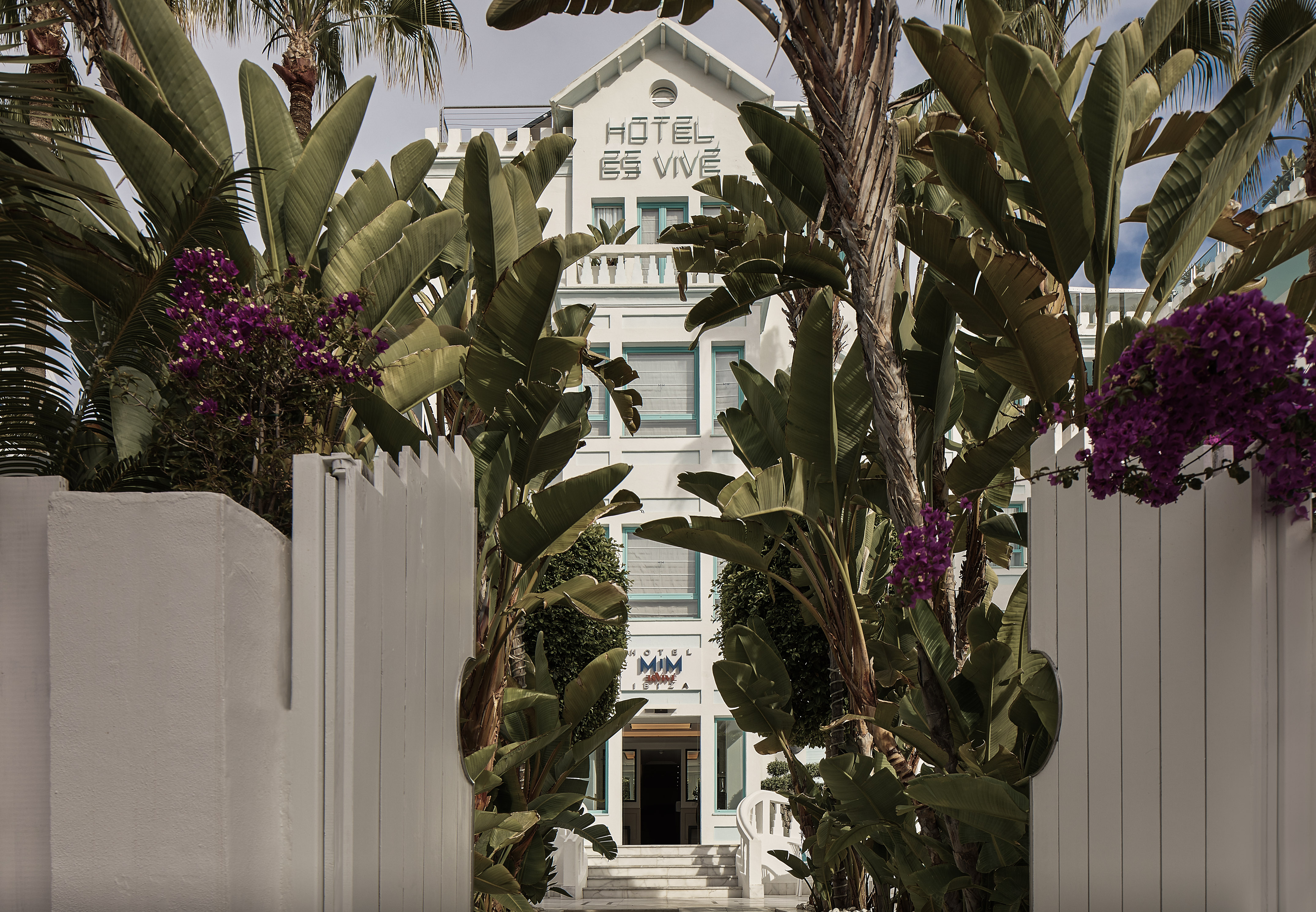 a white building with palm trees and a white fence