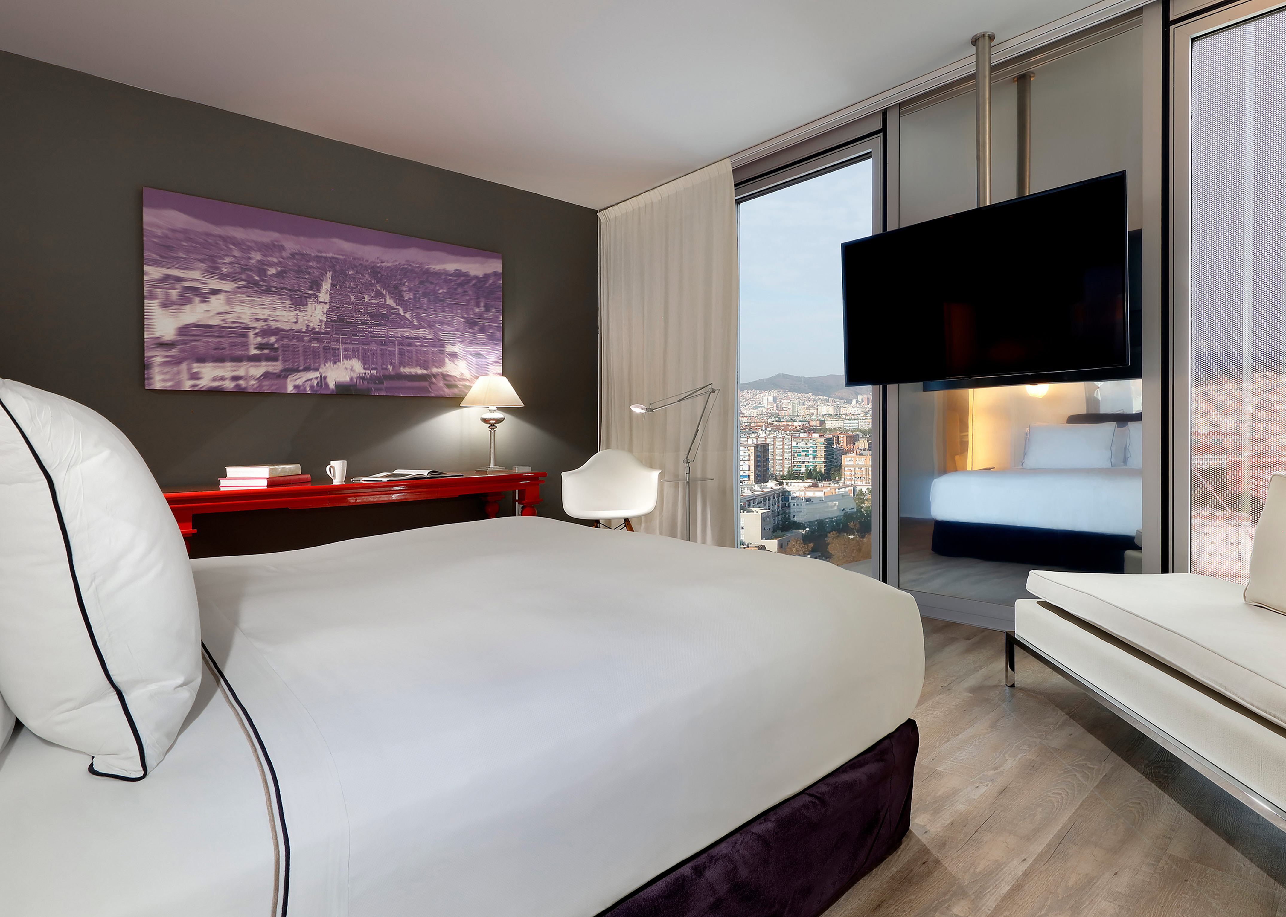 Modern hotel room with city view, large bed, flat-screen TV, and work desk.