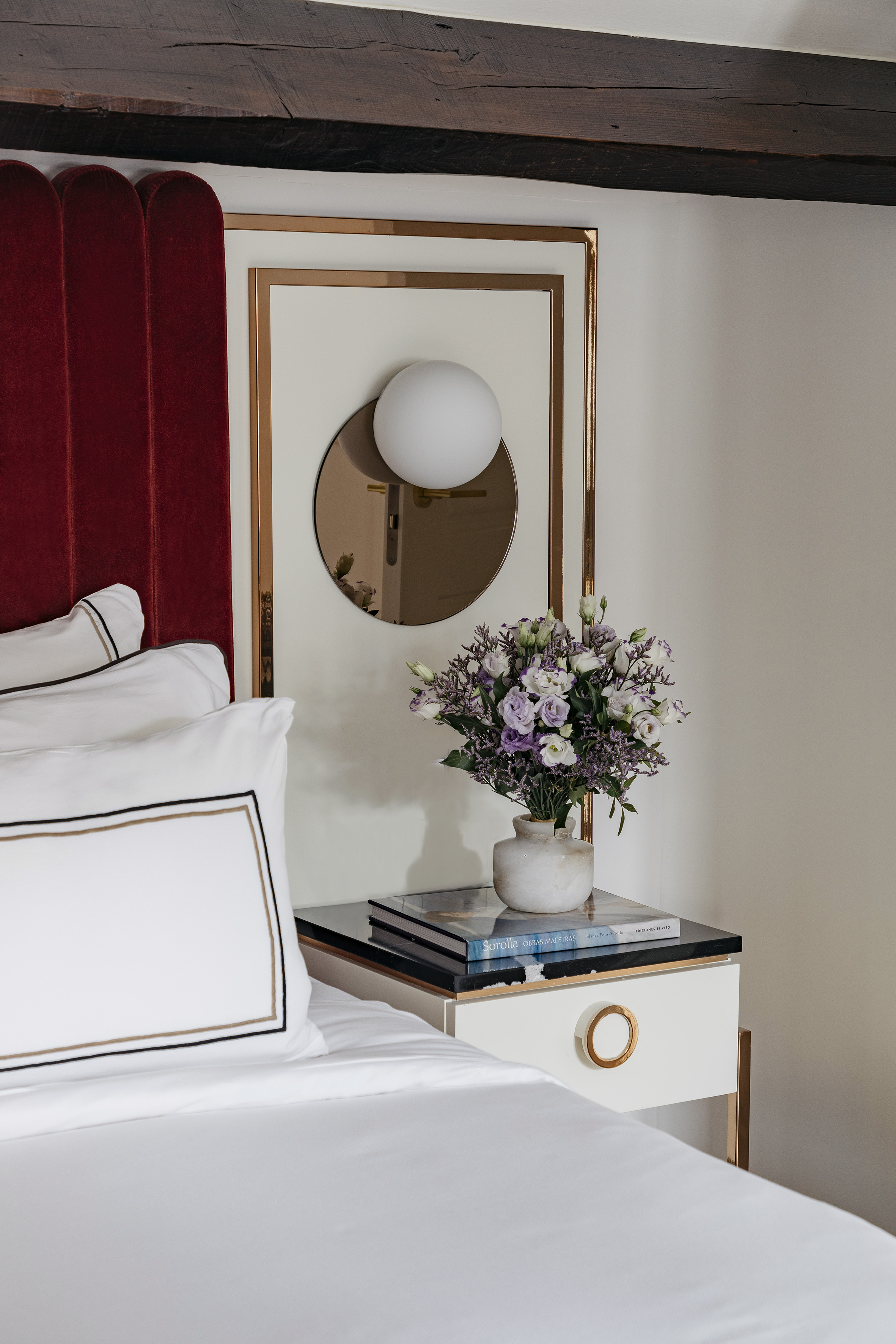 Luxury bedroom: red velvet headboard, modern nightstand, flowers, and white bedding.