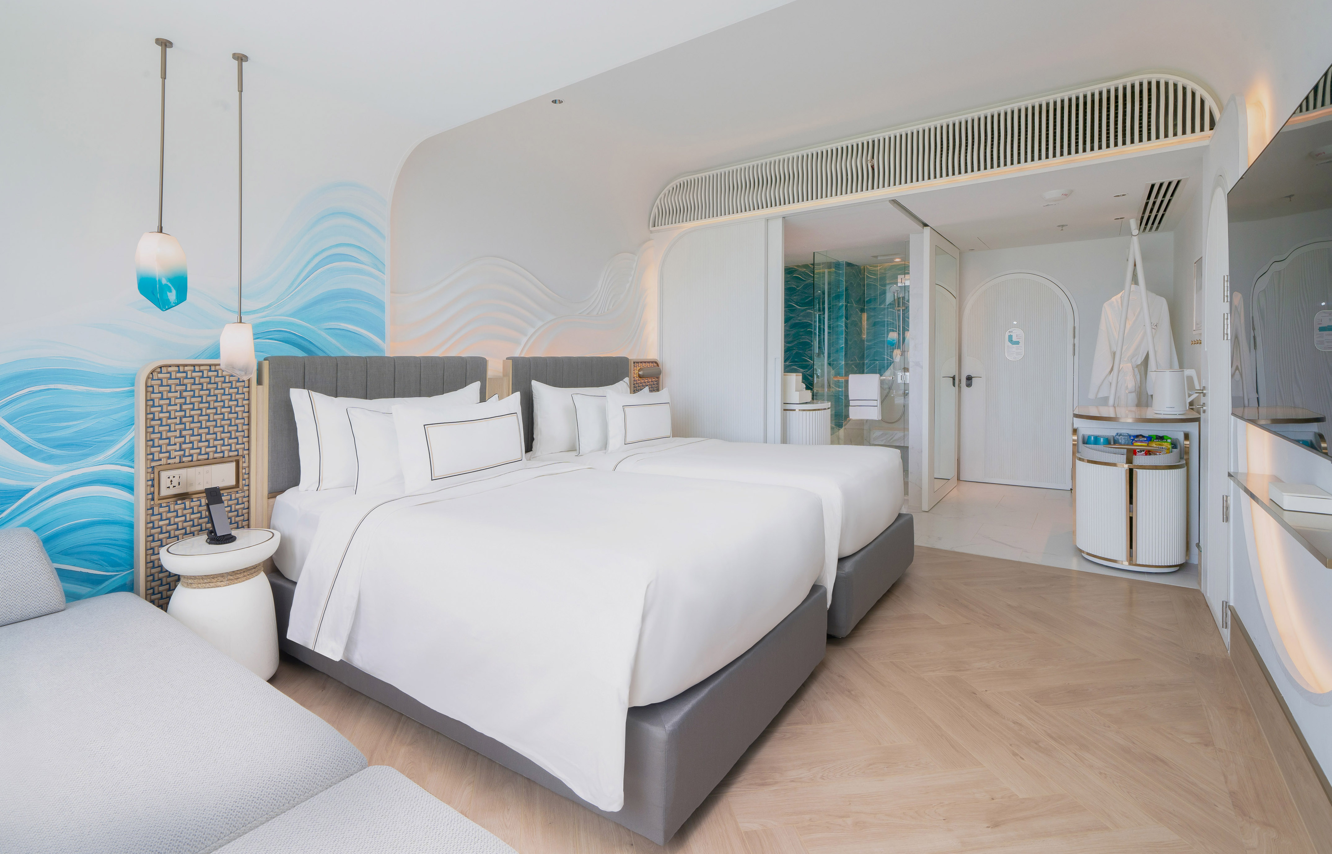 Bright hotel room with two twin beds, ocean wave mural, and modern amenities.