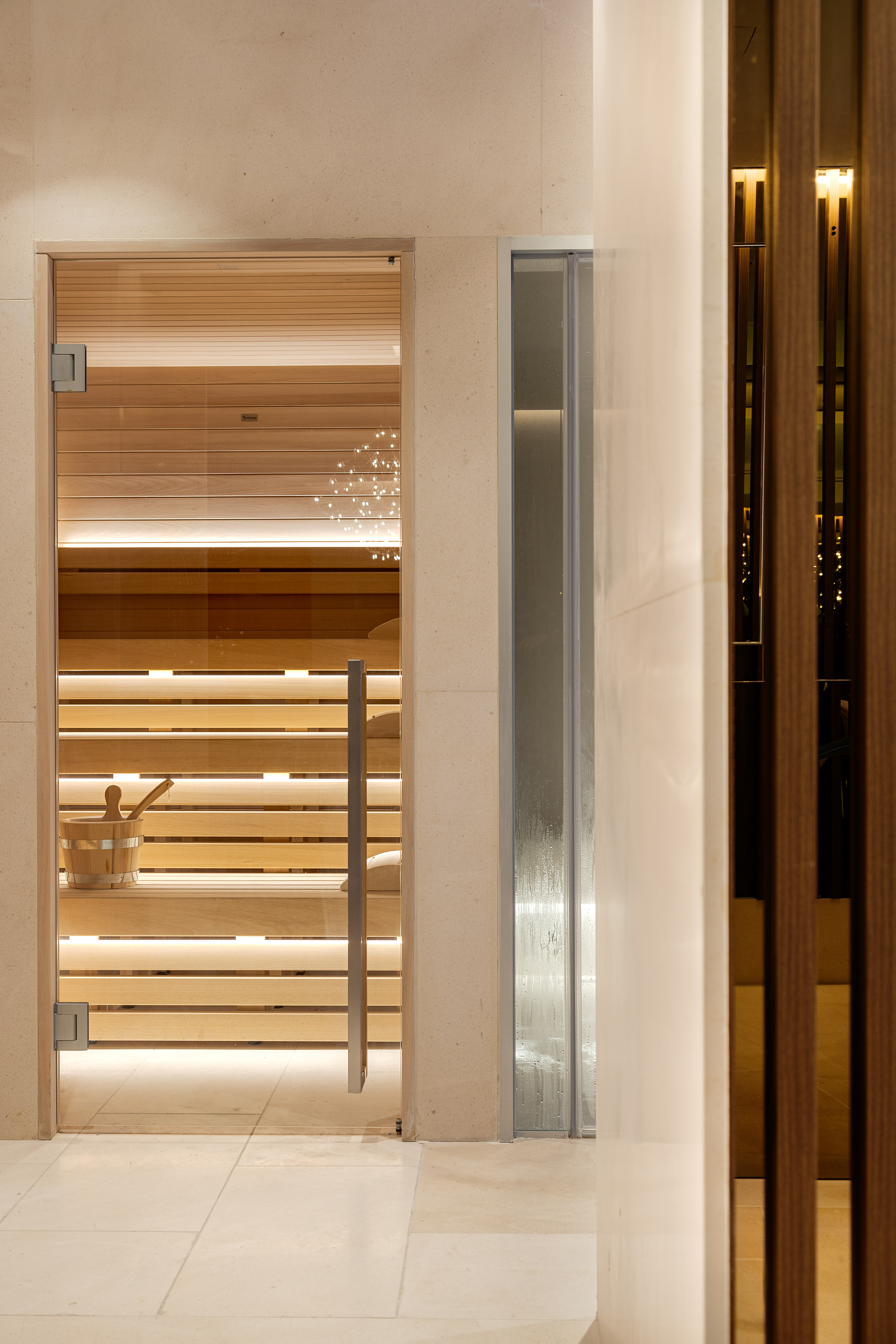 Modern spa sauna with glass door, light wood interior, LED lights, and shower.
