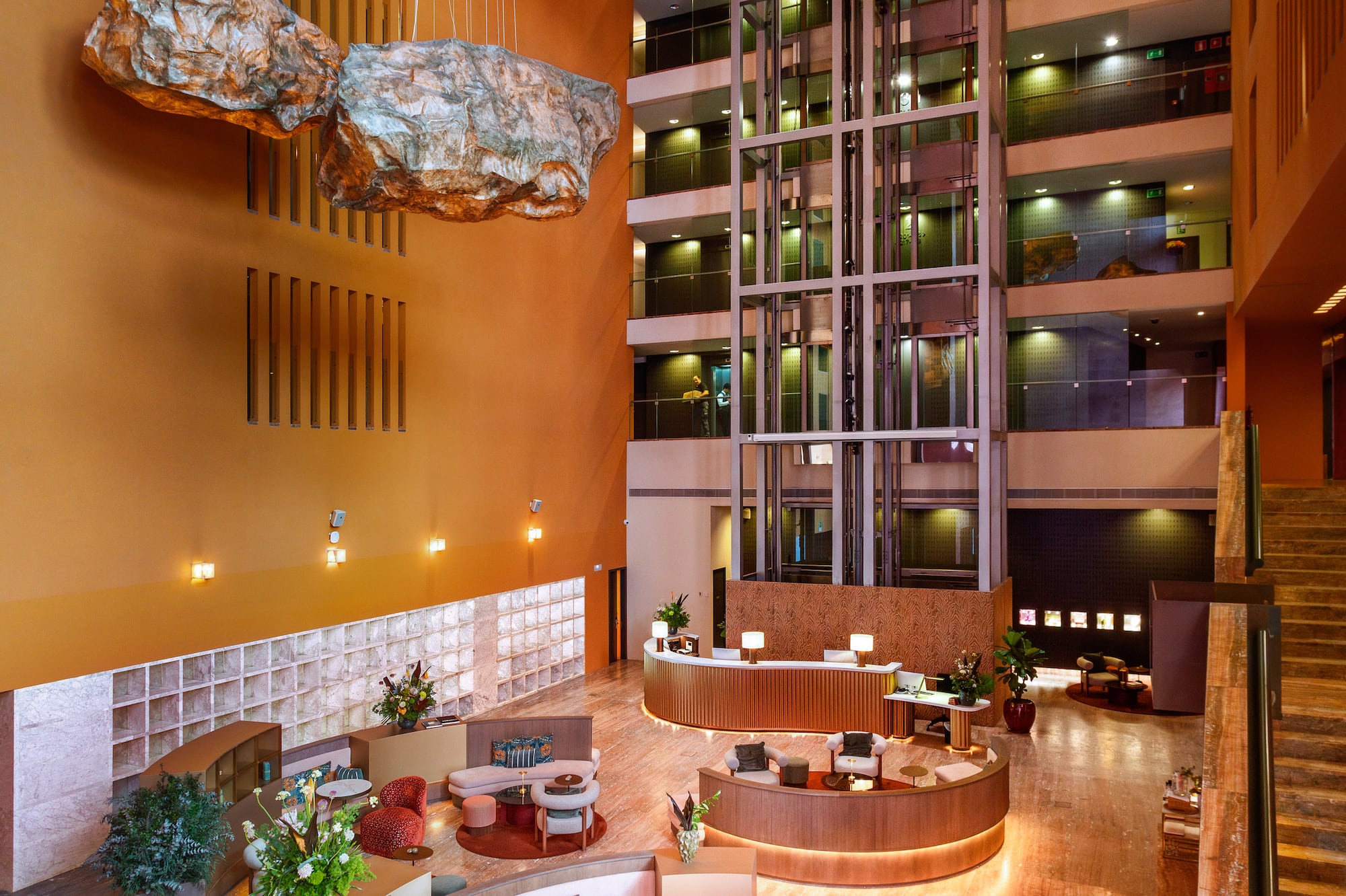 Hotel atrium with suspended rock decor, glass elevators, and stylish reception lounge.