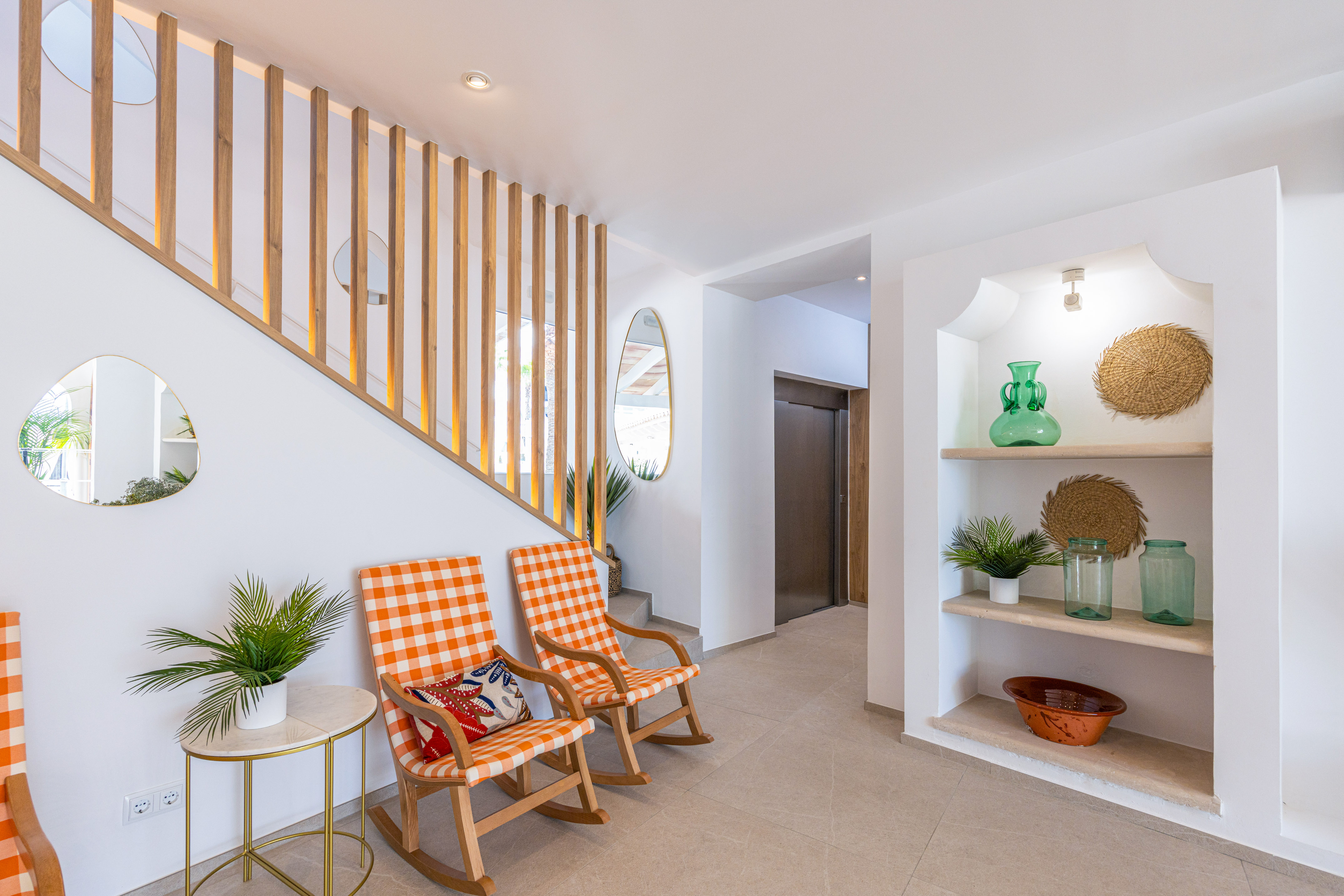 Modern hallway, wooden staircase, orange rocking chairs, built-in decor shelves.