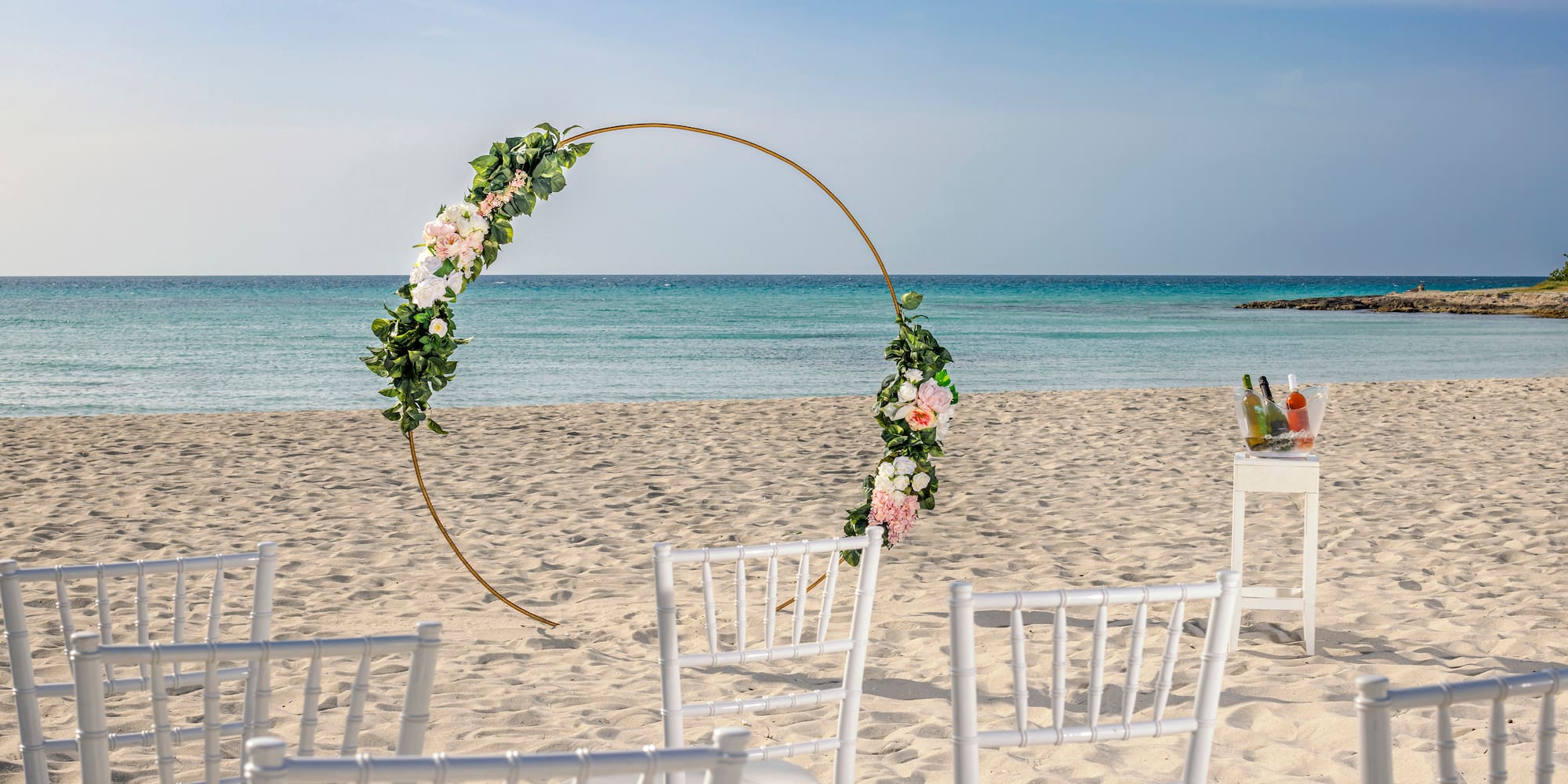 a beach with chairs and a table with drinks and a circular arch