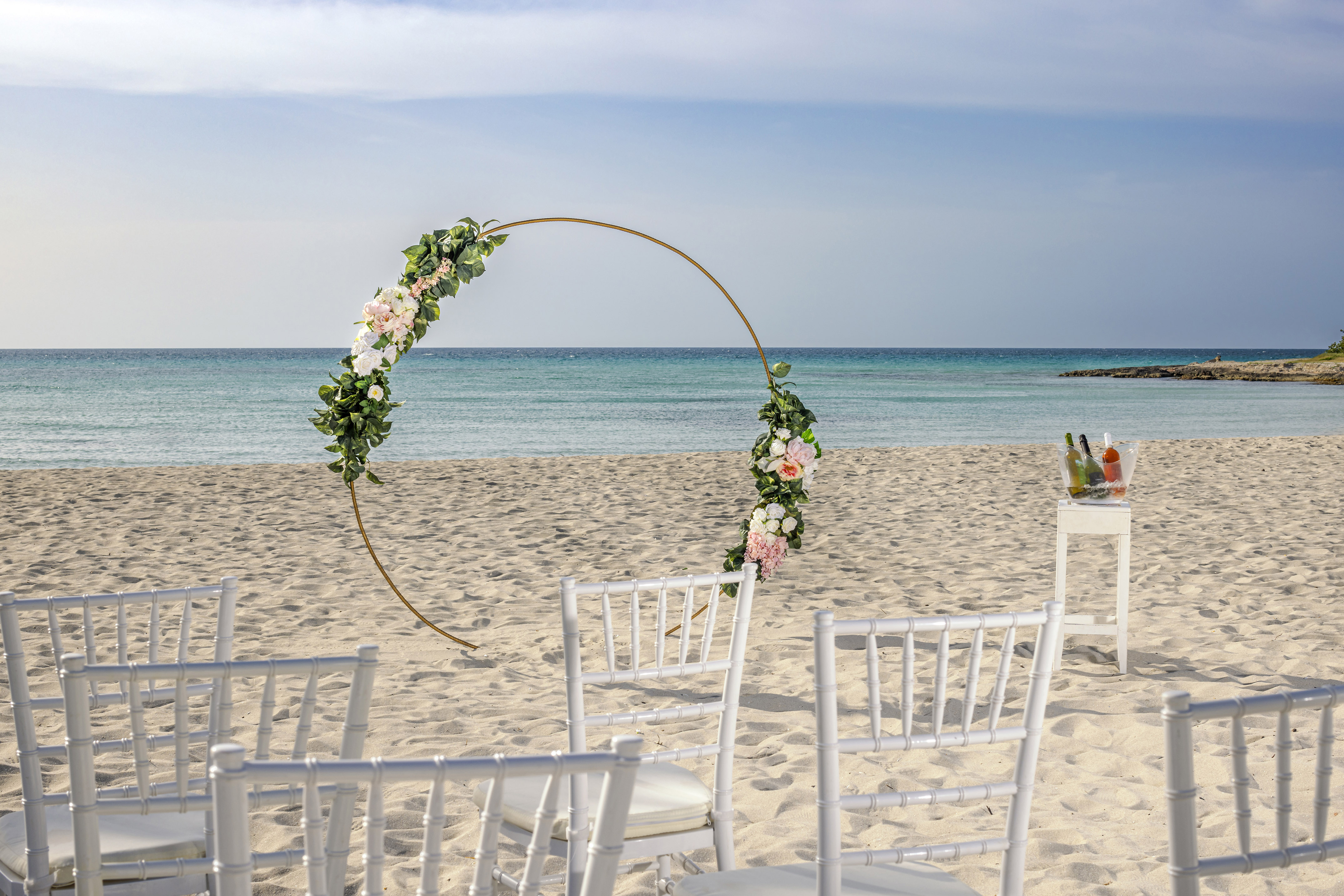 a beach with chairs and a table with drinks and a circular arch