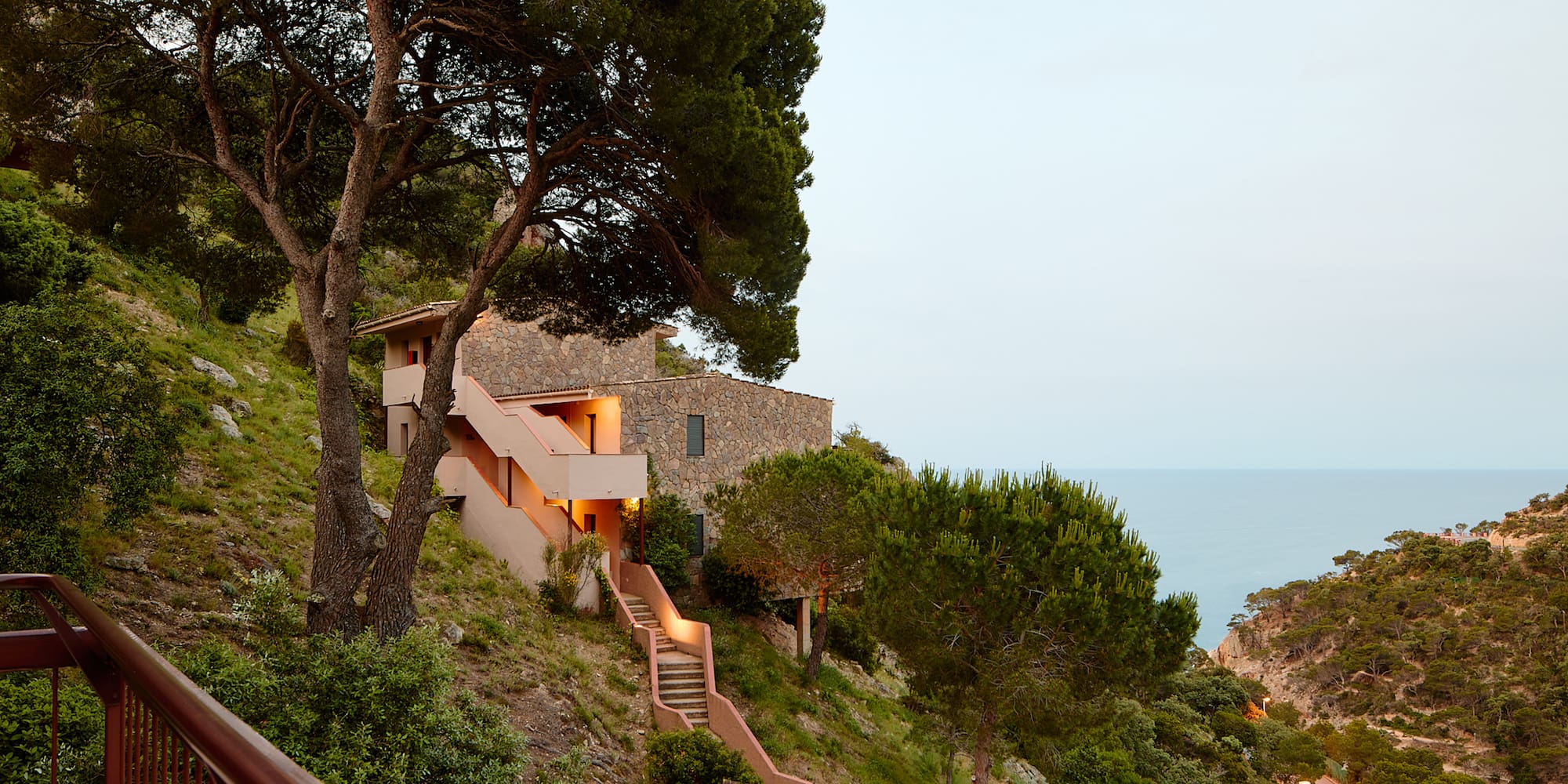 a building on a hill with trees and a railing