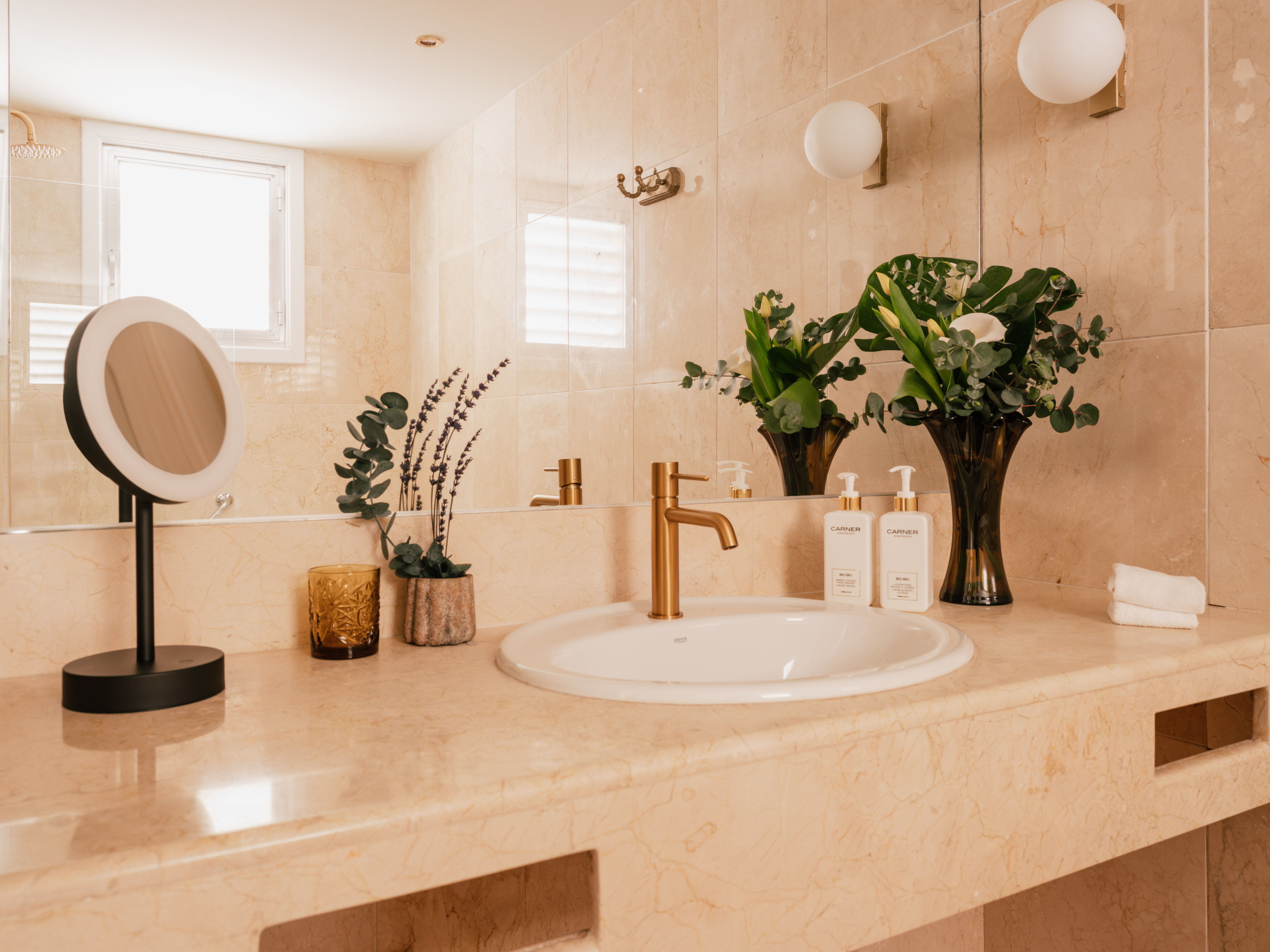 Modern marble bathroom vanity with gold faucet, sink, mirror, and plants.