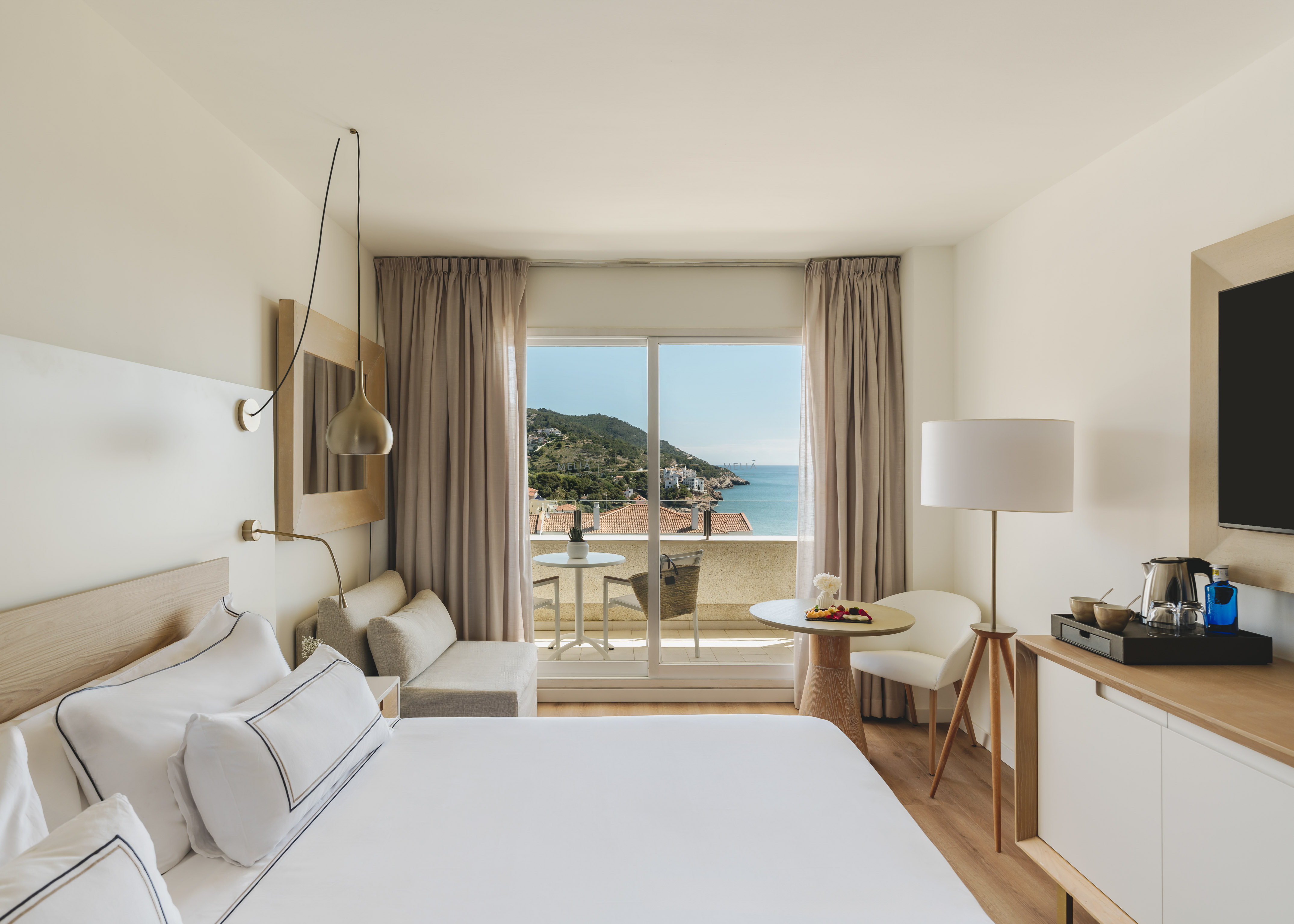 Modern hotel room with sea view balcony overlooking a coastal town.