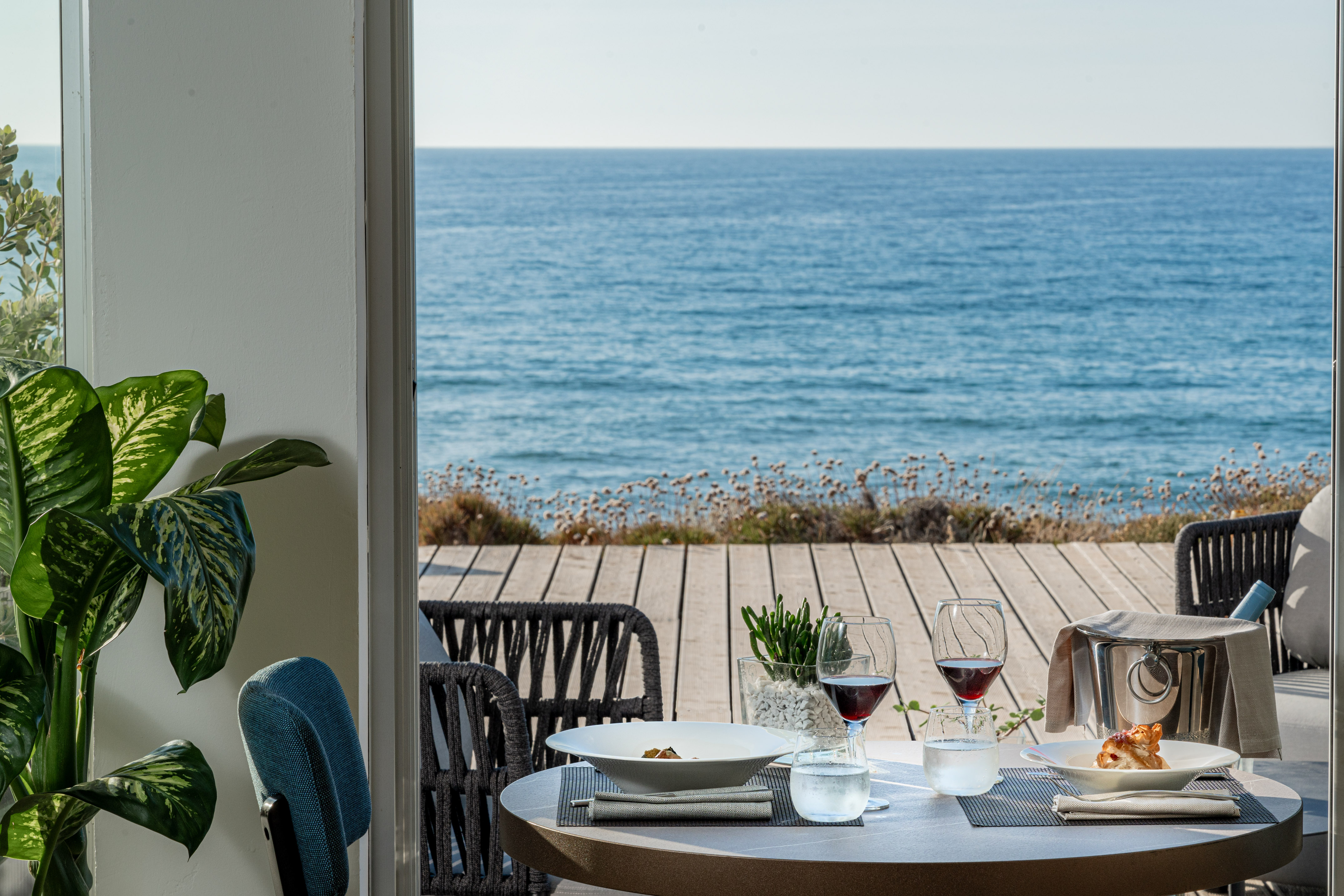 Oceanfront restaurant table with food, wine, and a stunning blue sea view.