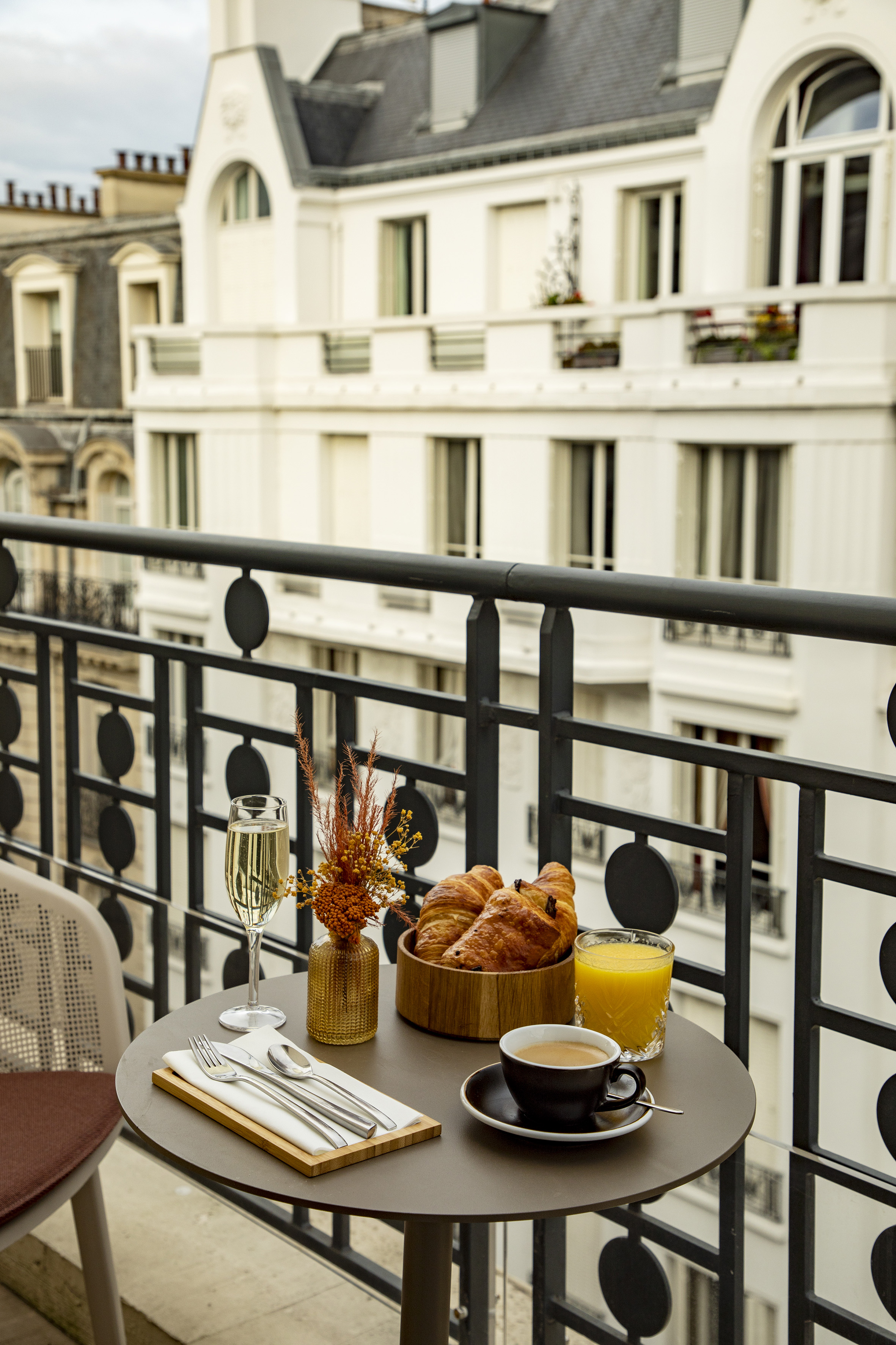 Balcony breakfast with croissants, coffee, champagne, orange juice, cityscape.