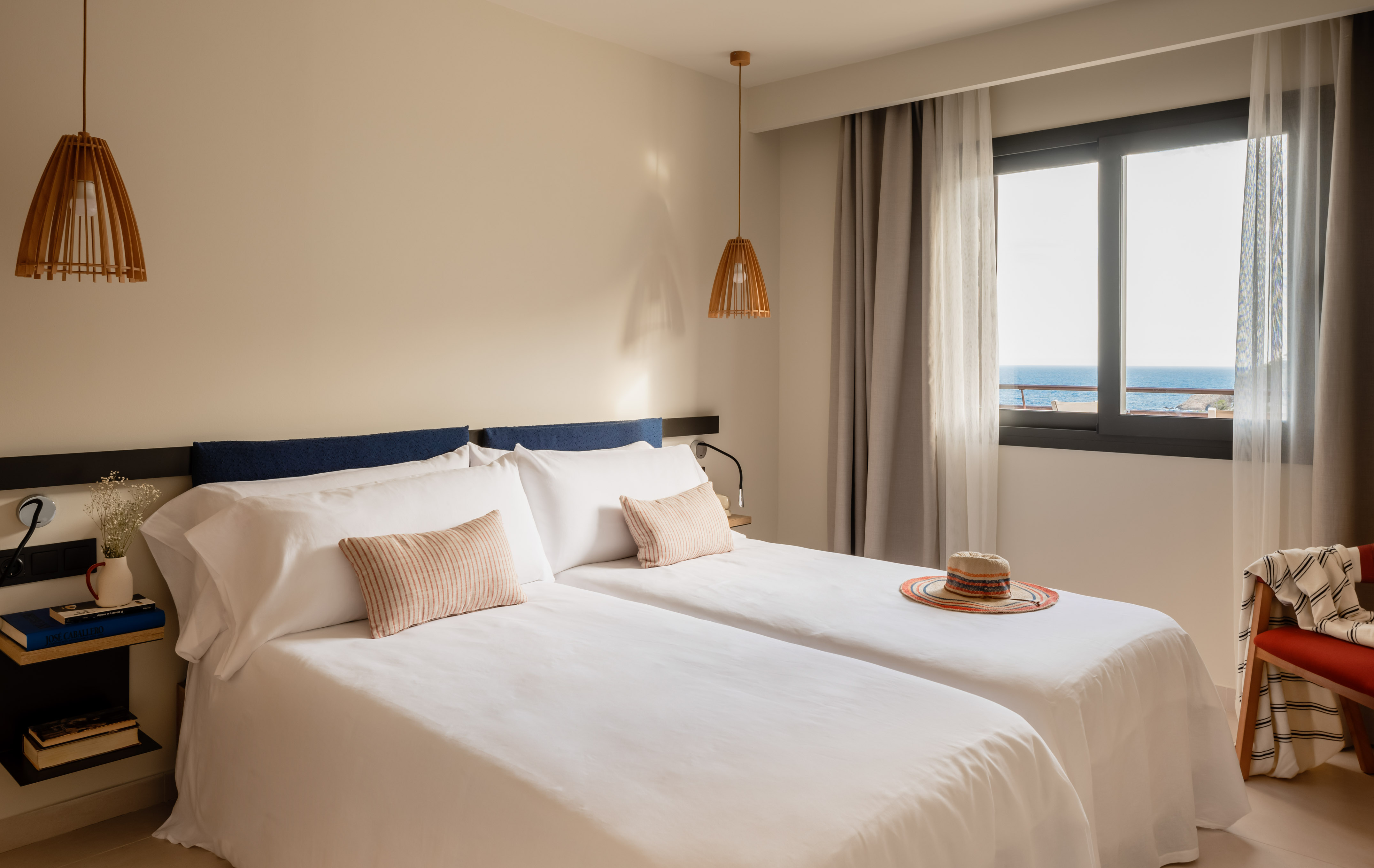 Hotel twin bedroom with direct ocean view, white beds, and natural wooden decor.