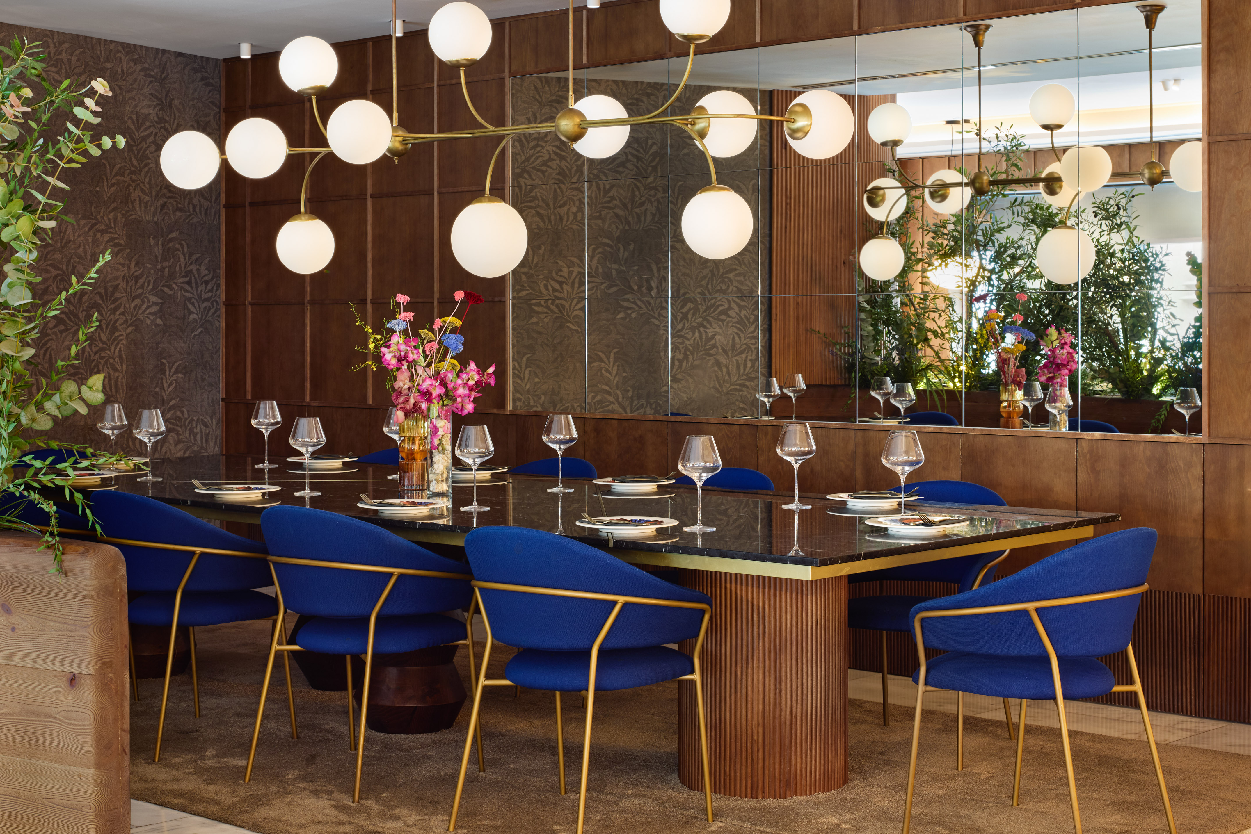 Elegant restaurant dining room with blue chairs, gold chandelier, and wood paneling.
