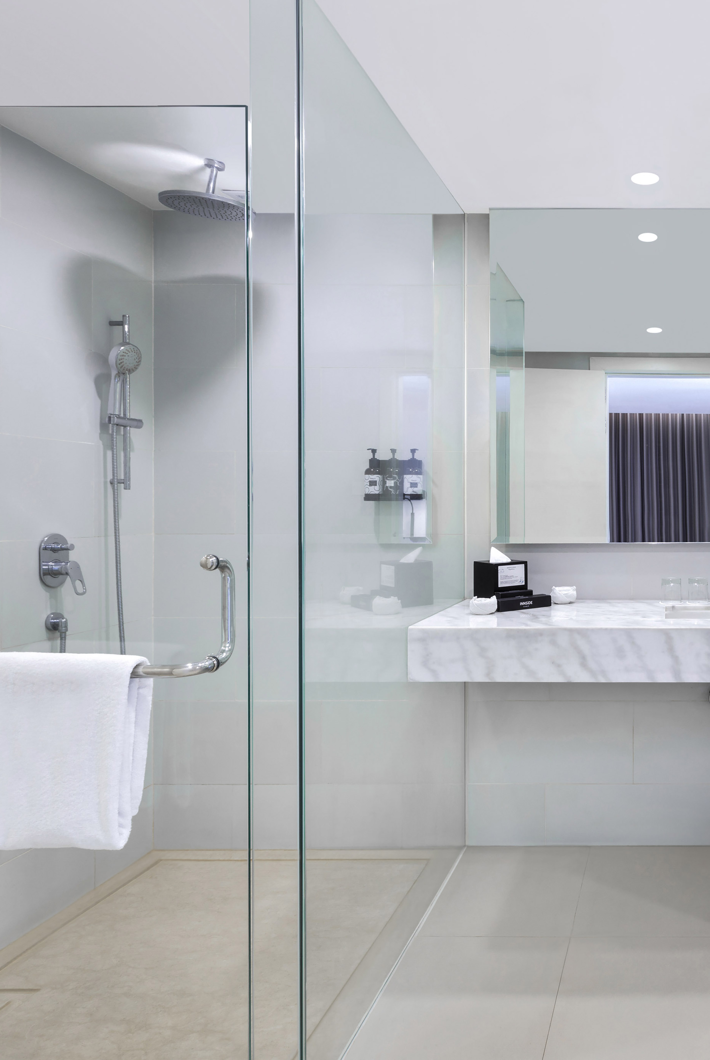 Modern hotel bathroom with glass shower, rain showerhead, and marble vanity.