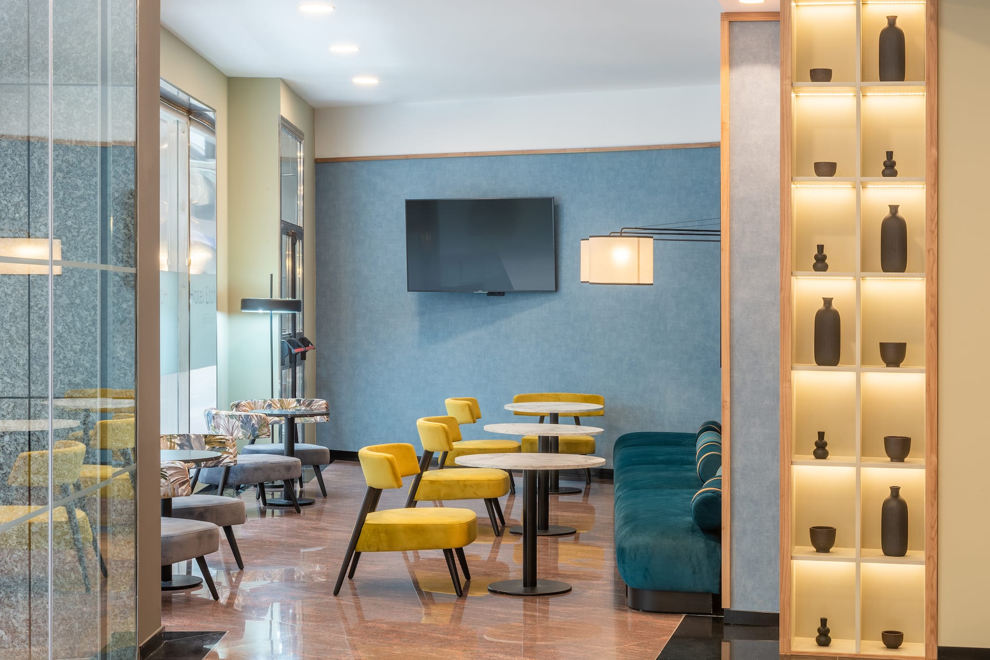 Contemporary lounge with yellow chairs, teal sofa, and illuminated shelving.