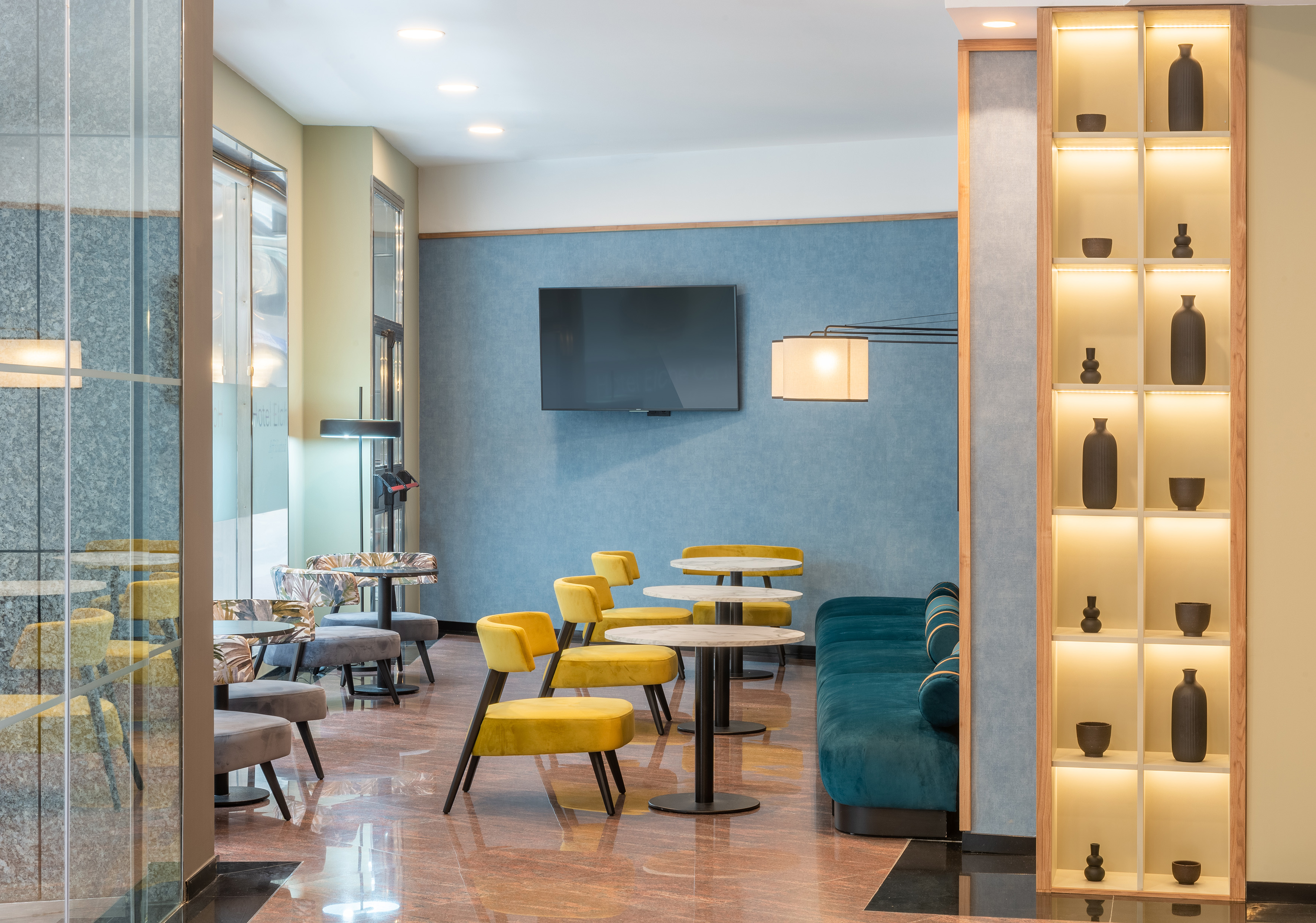 Contemporary lounge with yellow chairs, teal sofa, and illuminated shelving.
