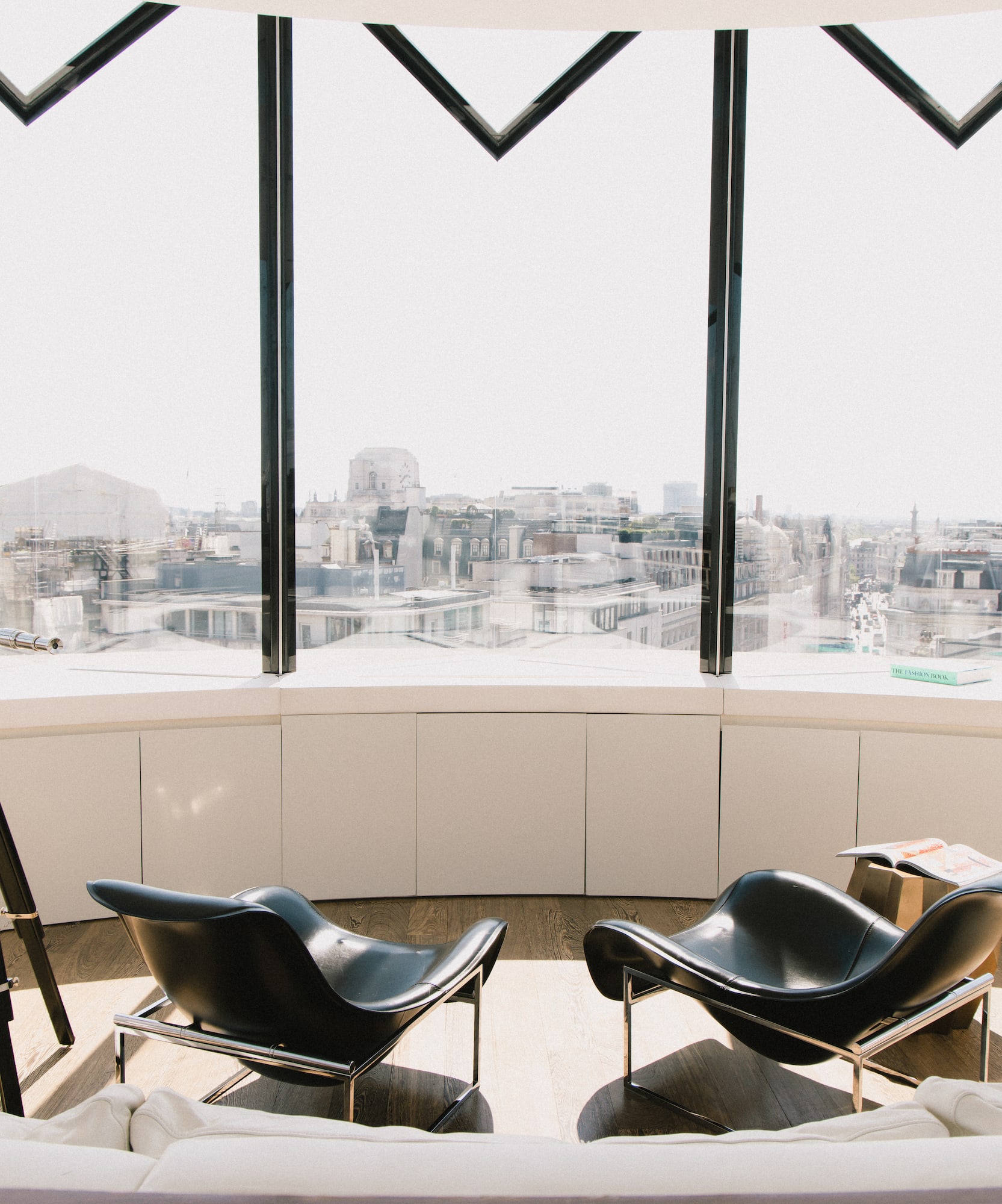 Modern lounge with black chairs, telescope, and city skyline view.