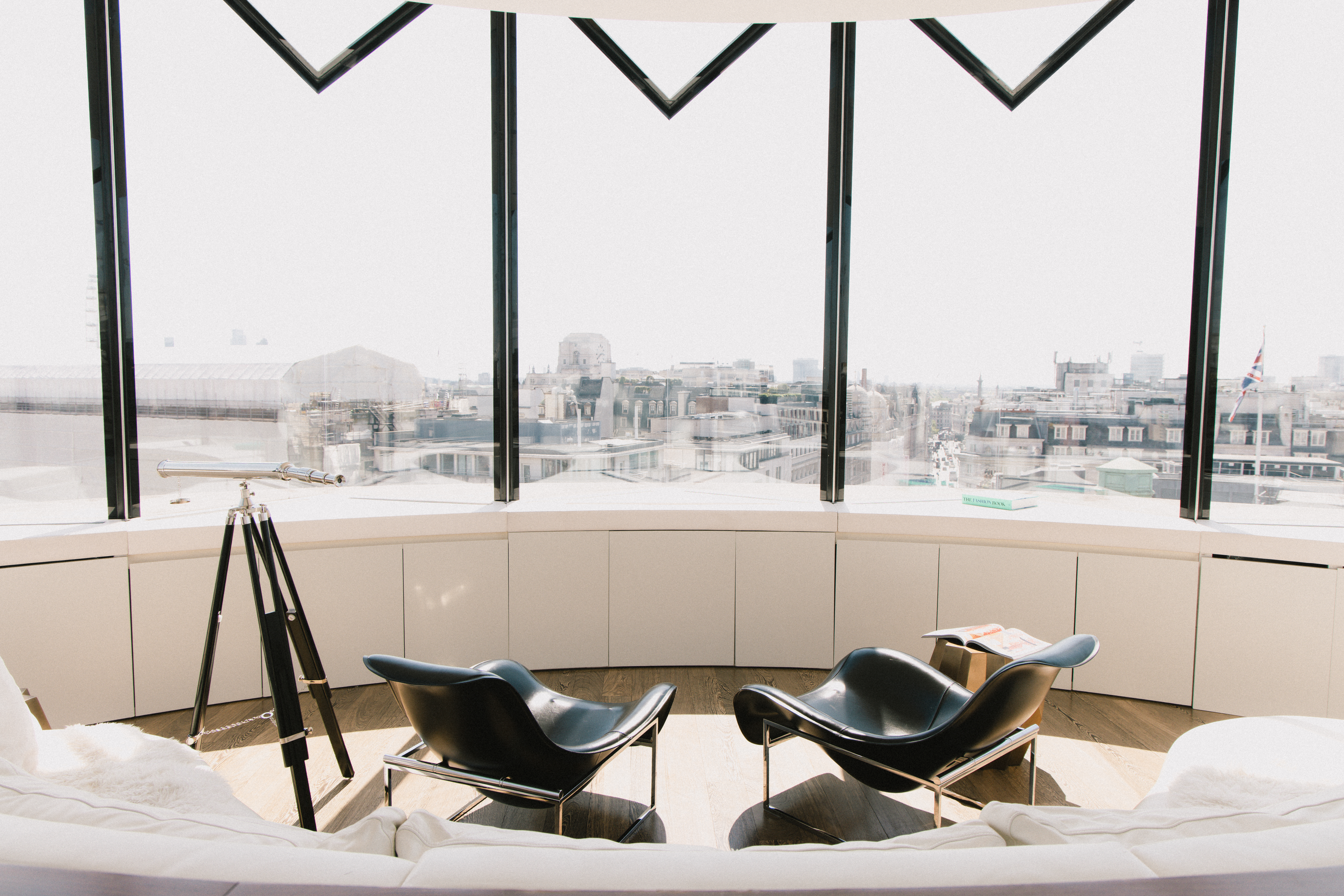 Modern lounge with black chairs, telescope, and city skyline view.