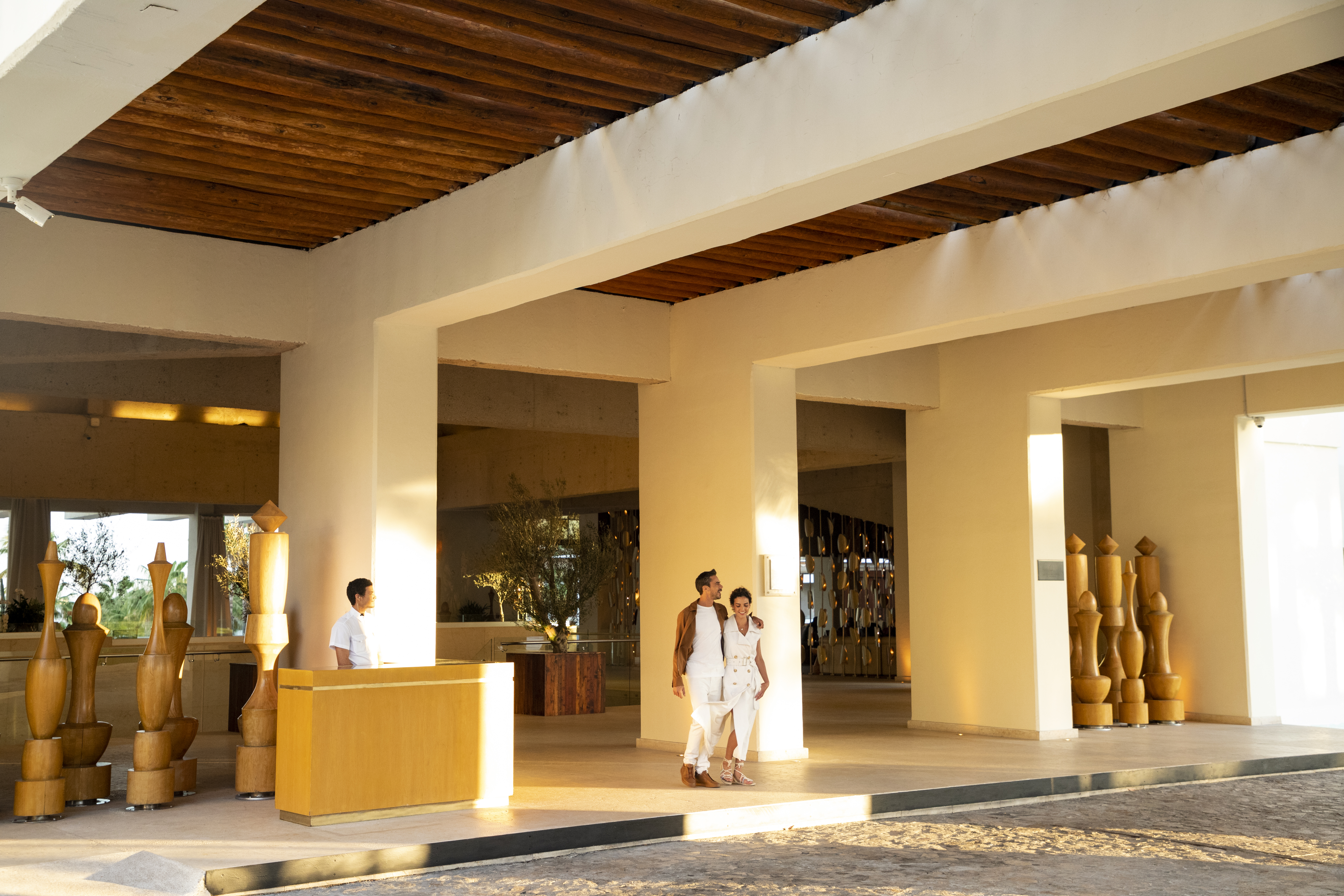 Spacious hotel lobby with couple, receptionist, and modern wooden ceiling.