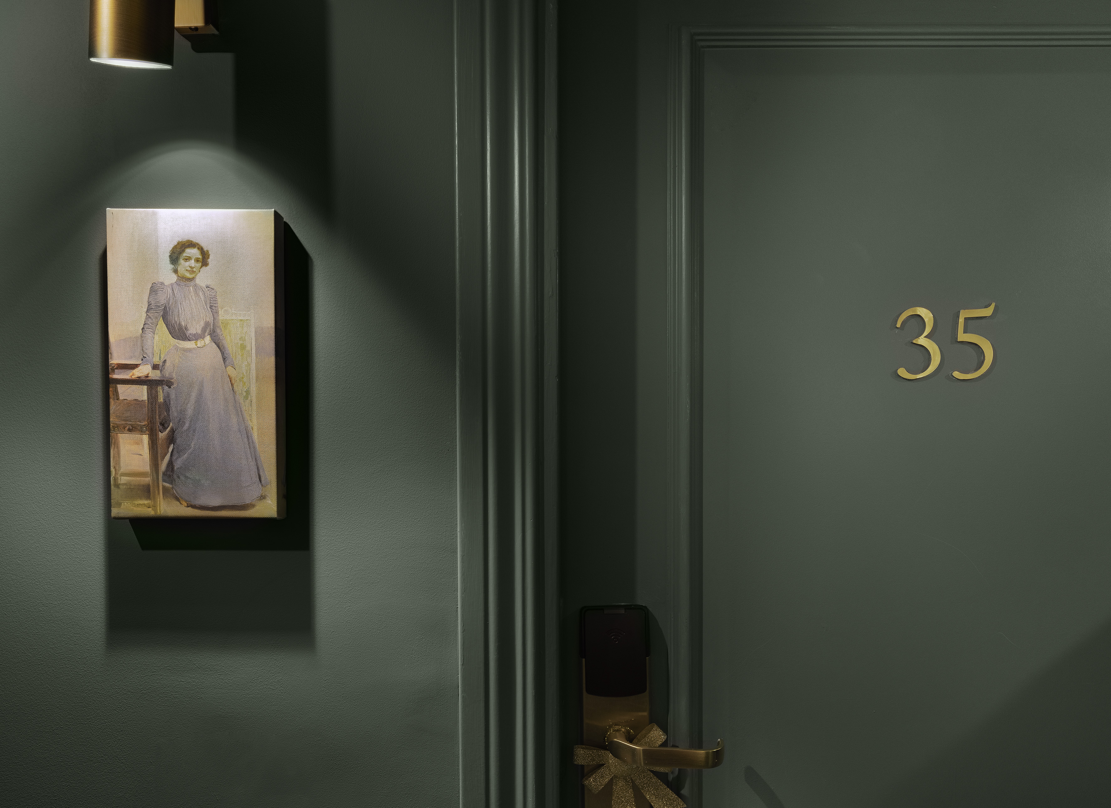 Dark green hotel door 35, gold accents, illuminated vintage portrait of a woman.