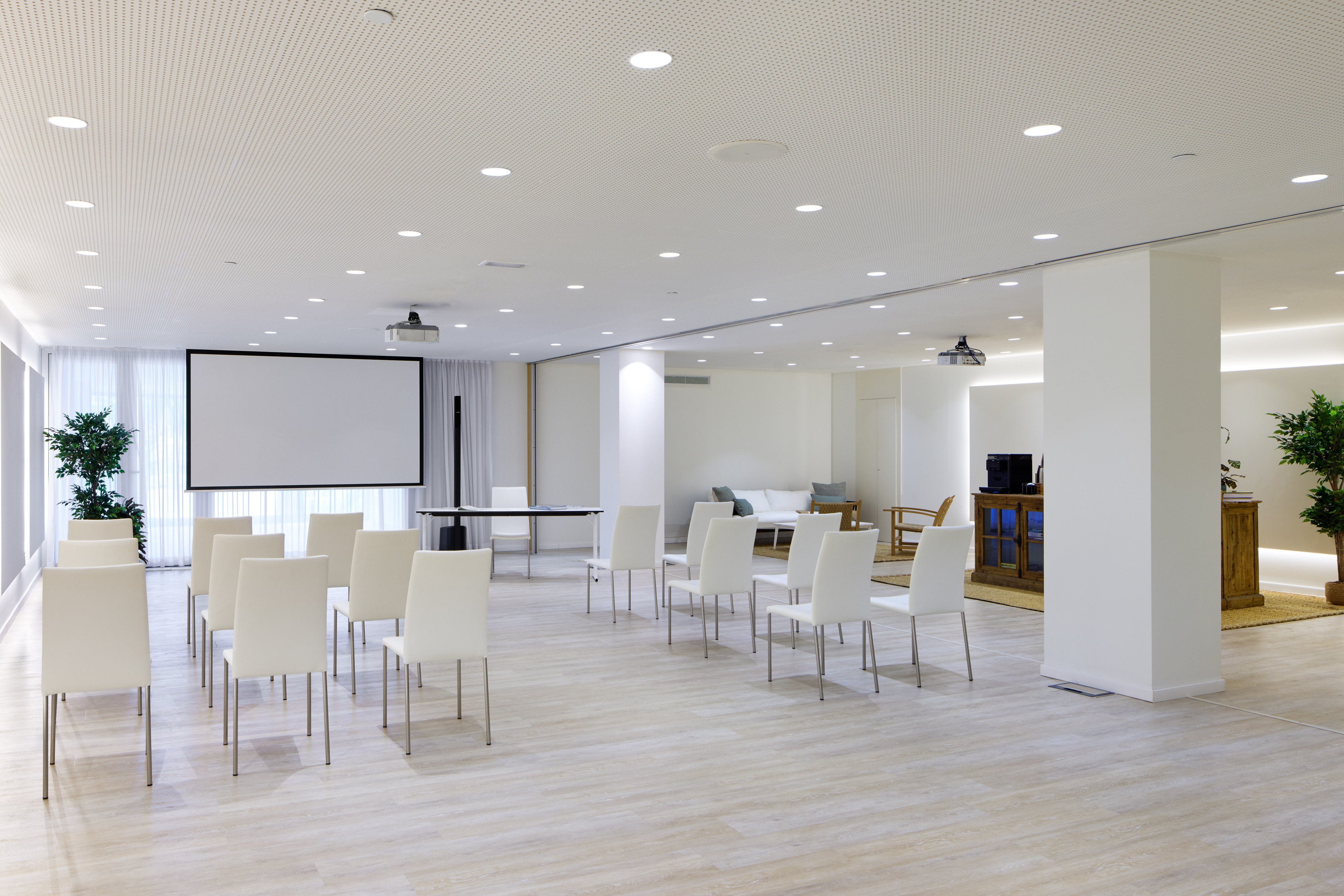 Bright corporate meeting room with white chairs and projector screen.