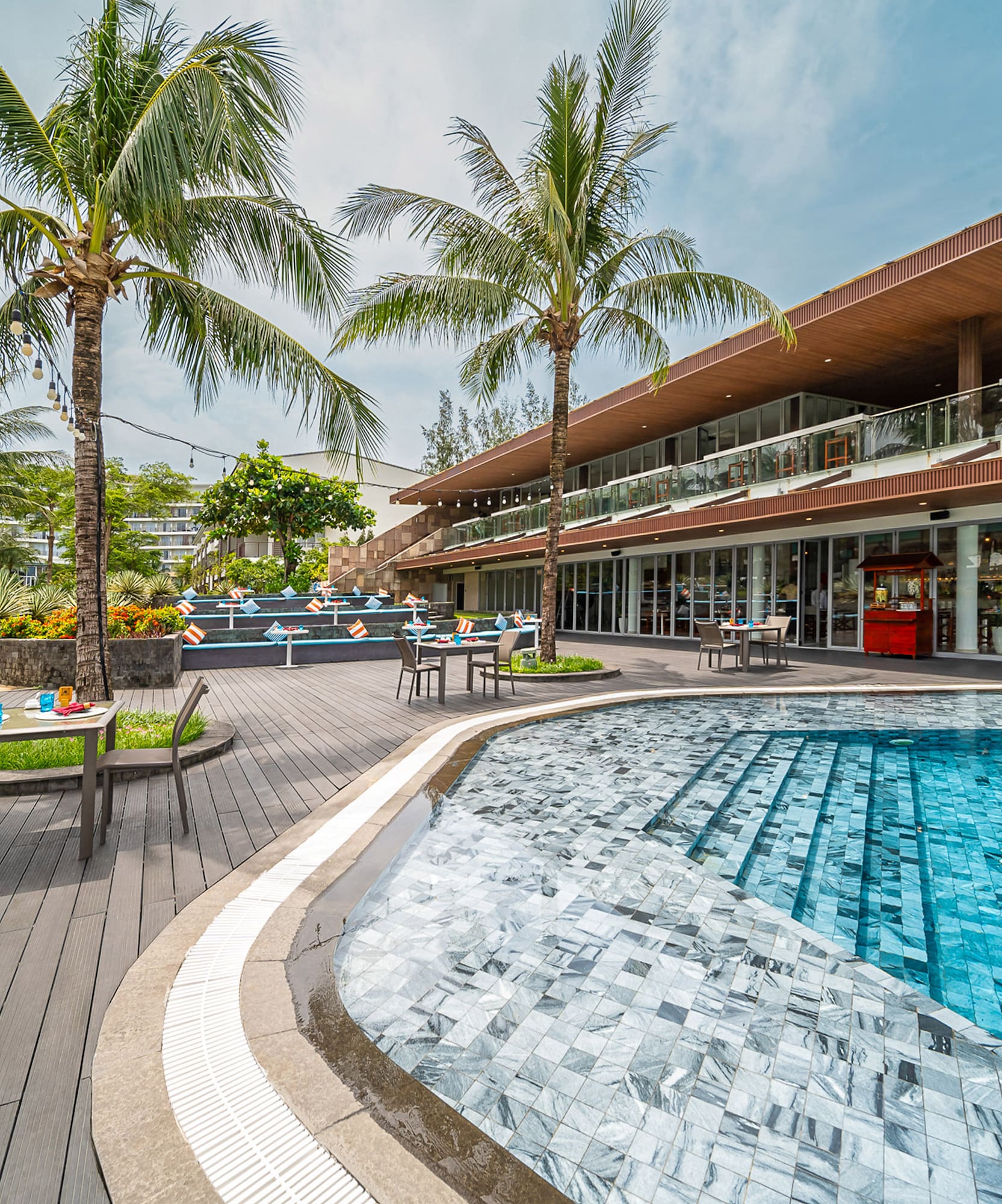 Tropical resort pool deck with modern hotel, palm trees, and outdoor lounge.