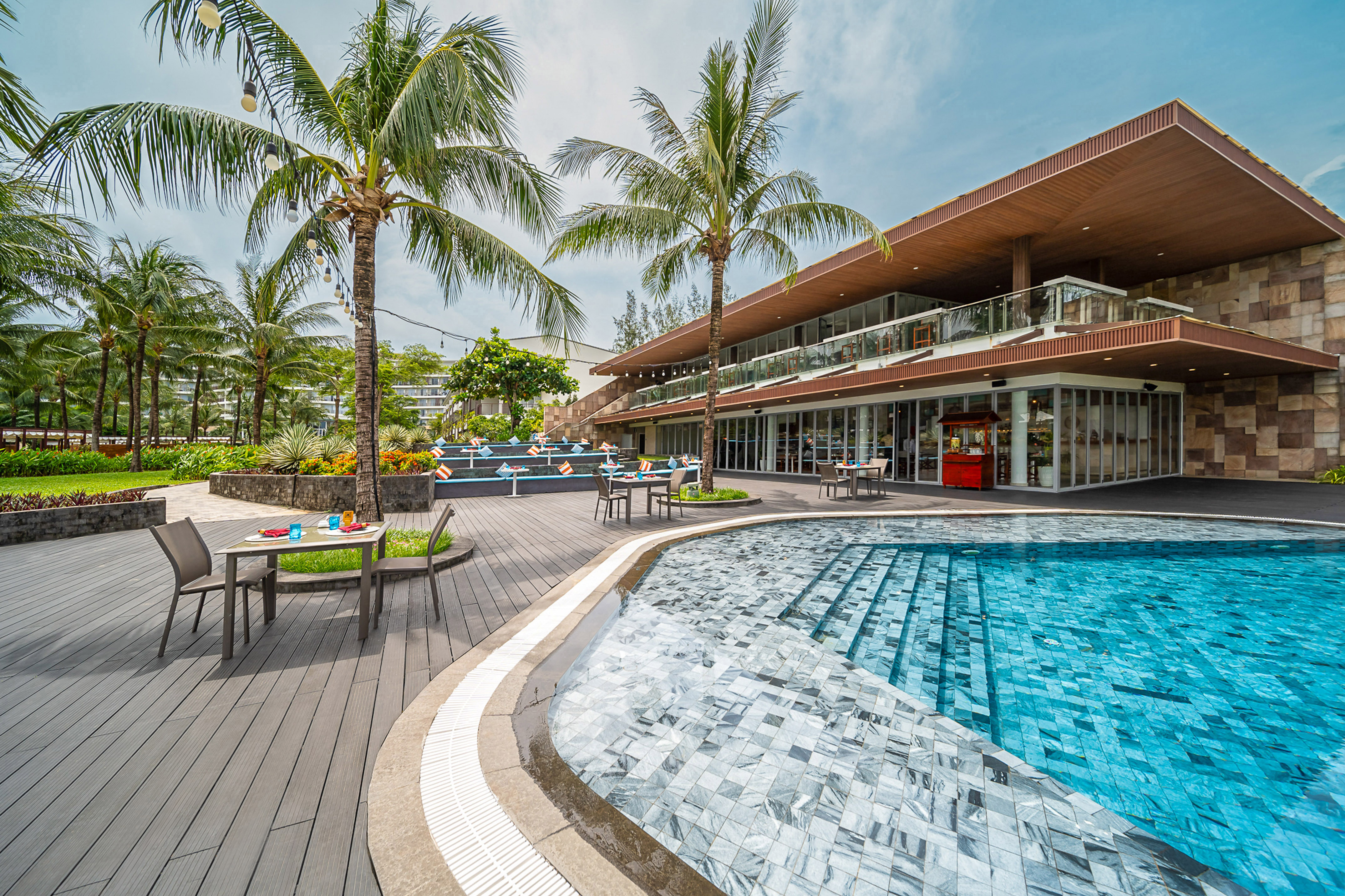Tropical resort pool deck with modern hotel, palm trees, and outdoor lounge.