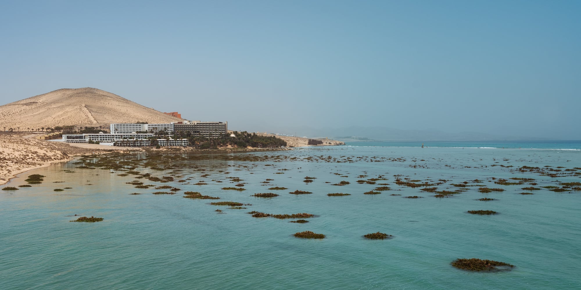 a body of water with a building and a hill in the background