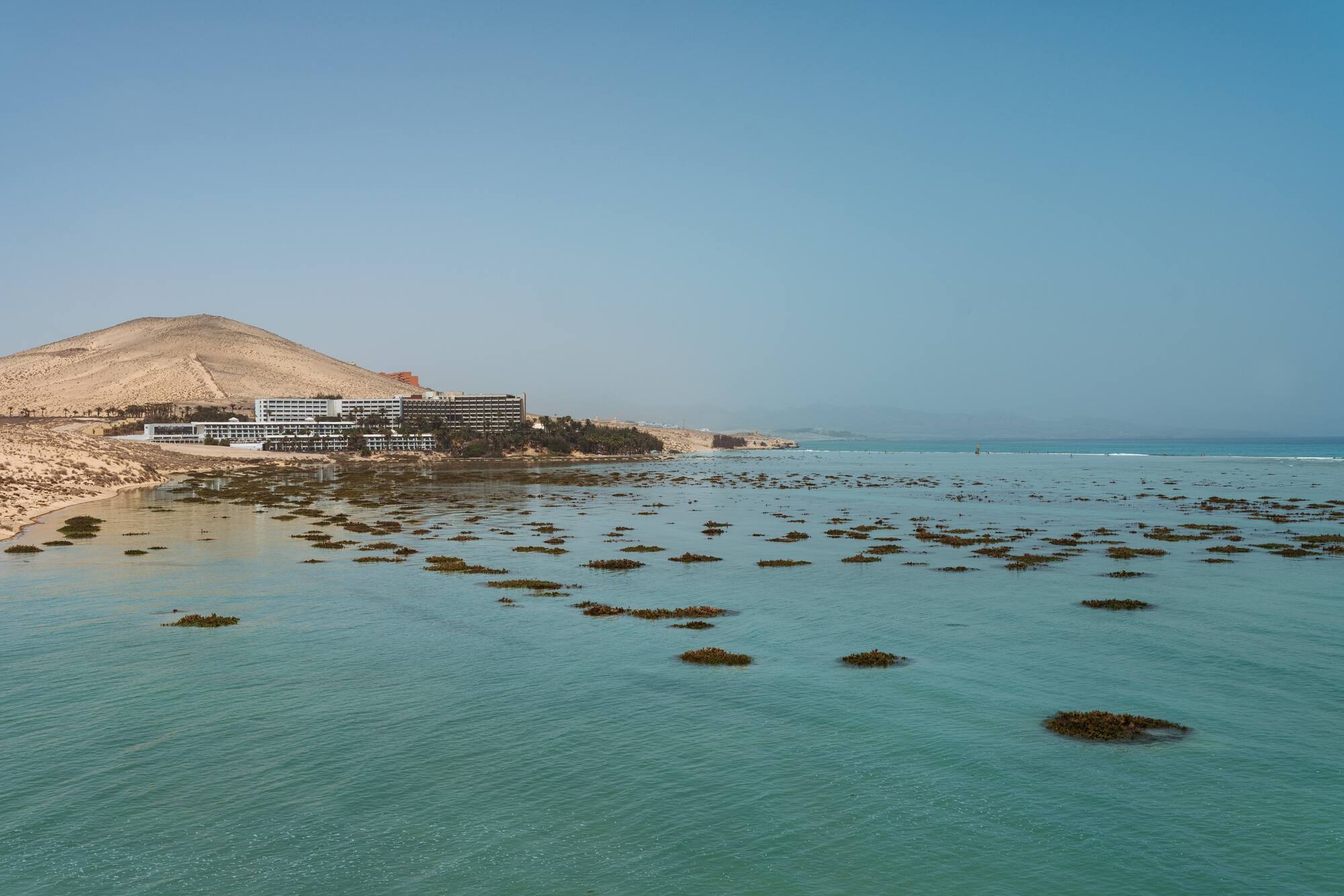 a body of water with a building and a hill in the background