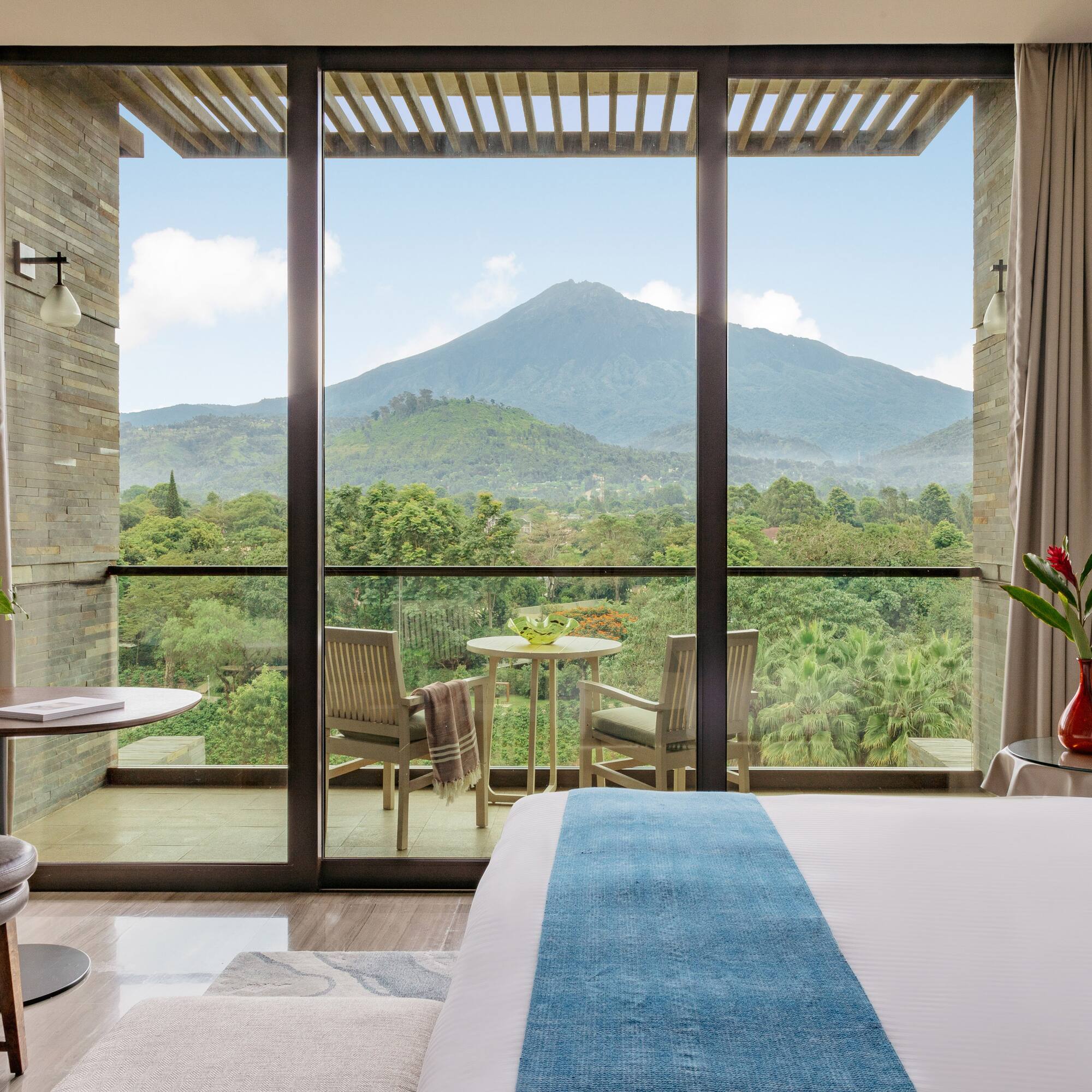 Modern hotel room with balcony, bed, and panoramic mountain view.