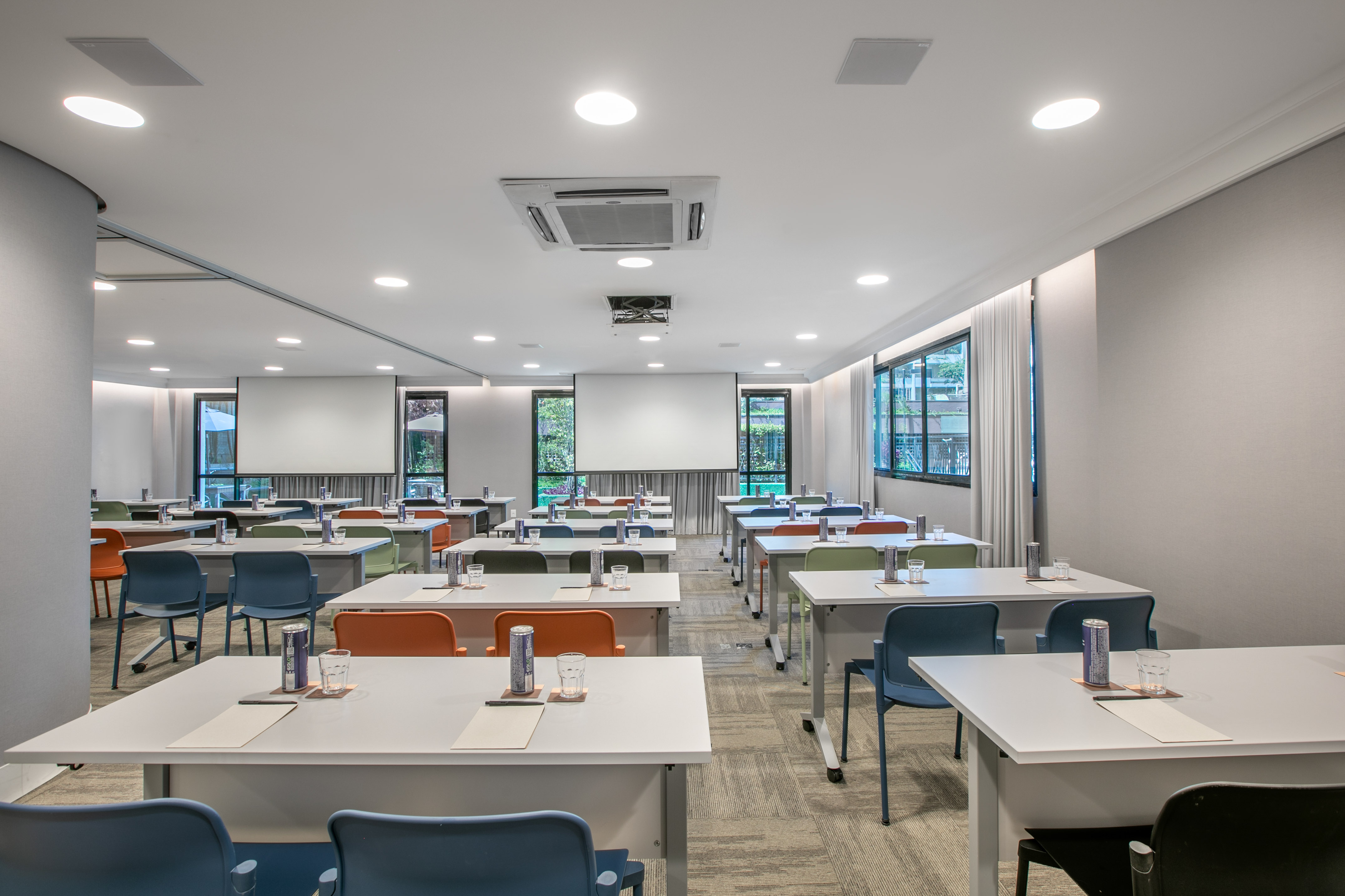 Modern training room with colorful chairs, tables, dual screens, and large windows.