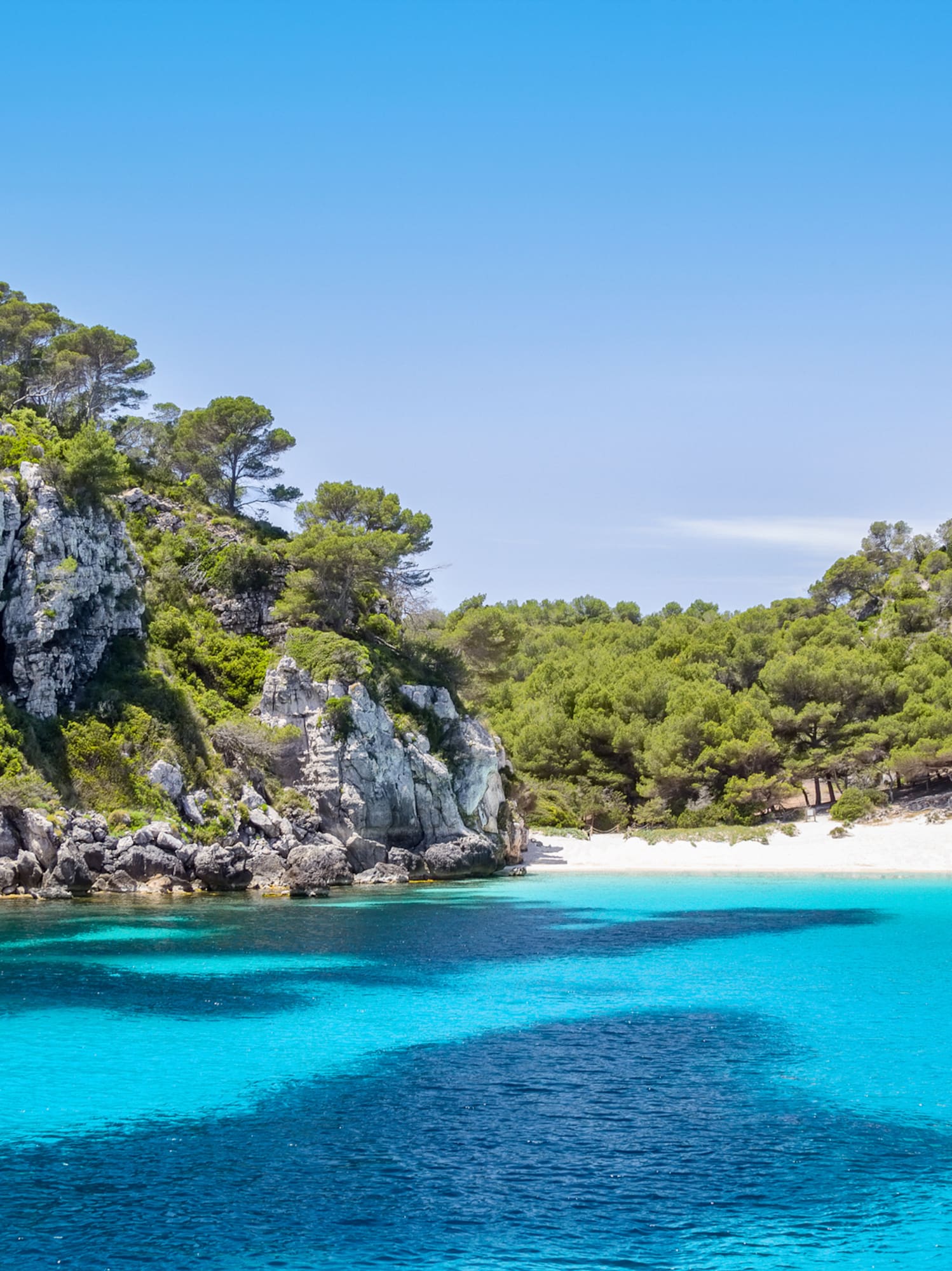 Crystal clear turquoise bay, white sand beach, and rocky pine cliffs.