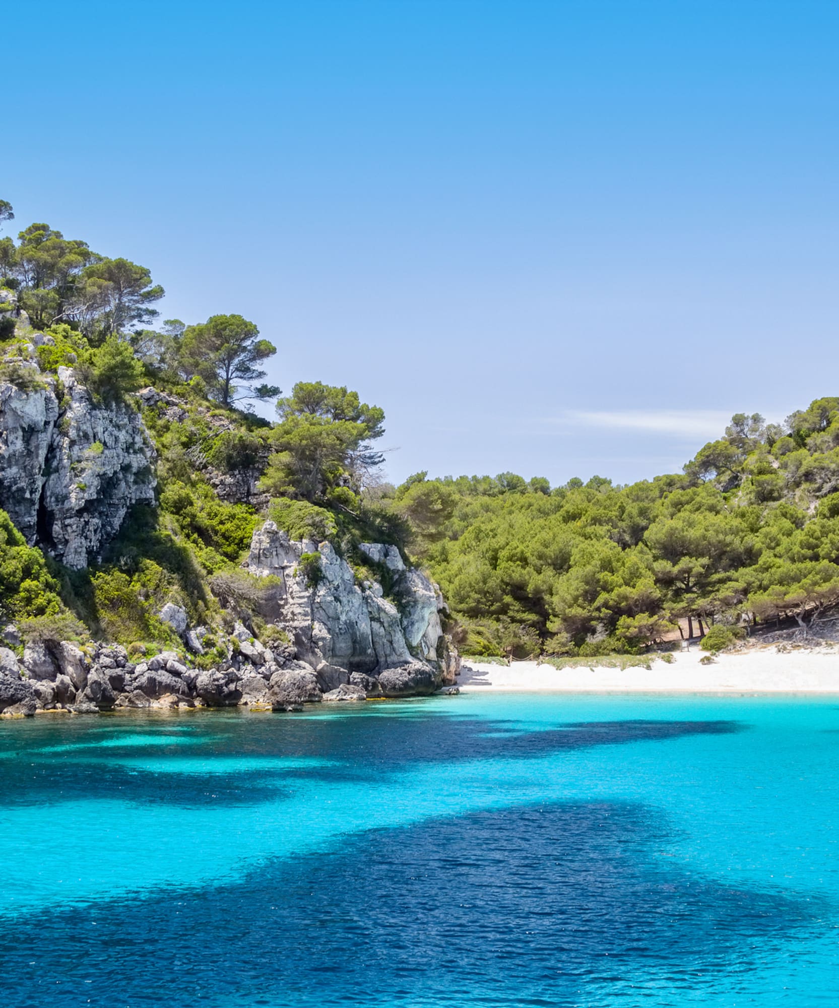 Crystal clear turquoise bay, white sand beach, and rocky pine cliffs.