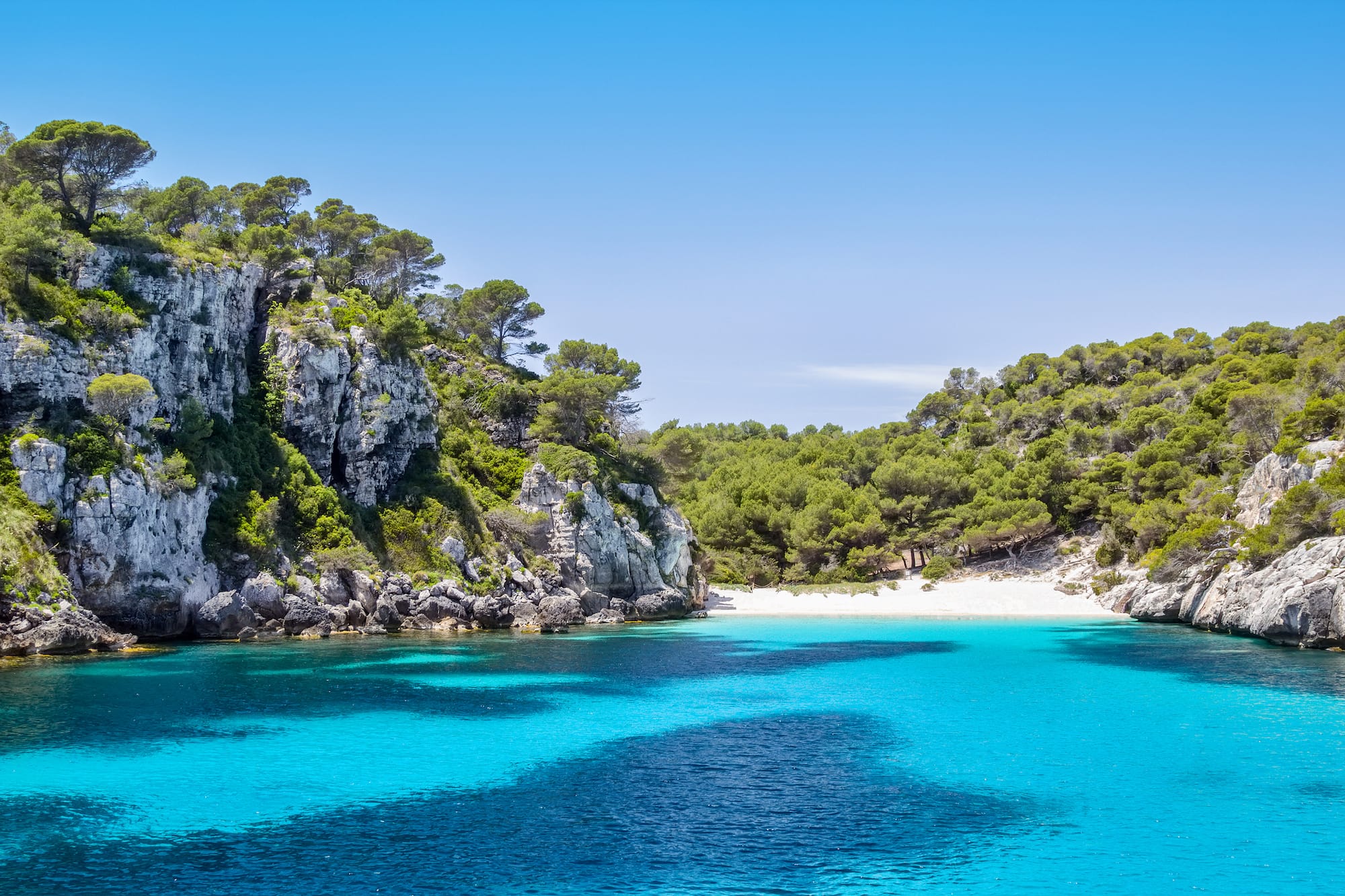 Crystal clear turquoise bay, white sand beach, and rocky pine cliffs.