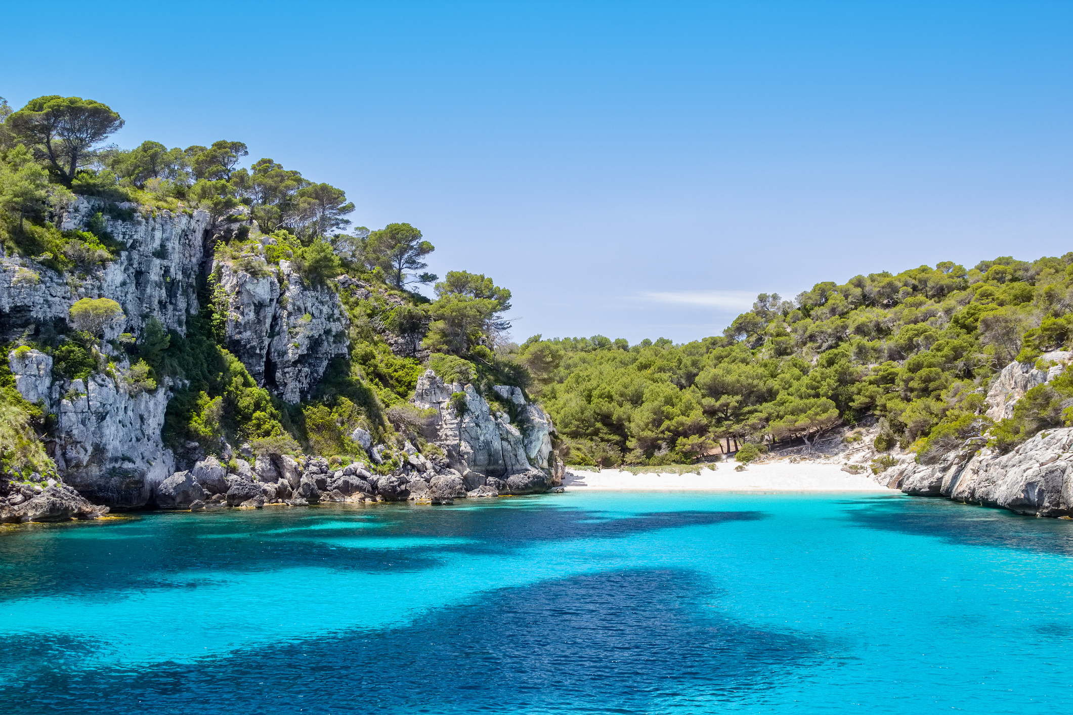 Crystal clear turquoise bay, white sand beach, and rocky pine cliffs.