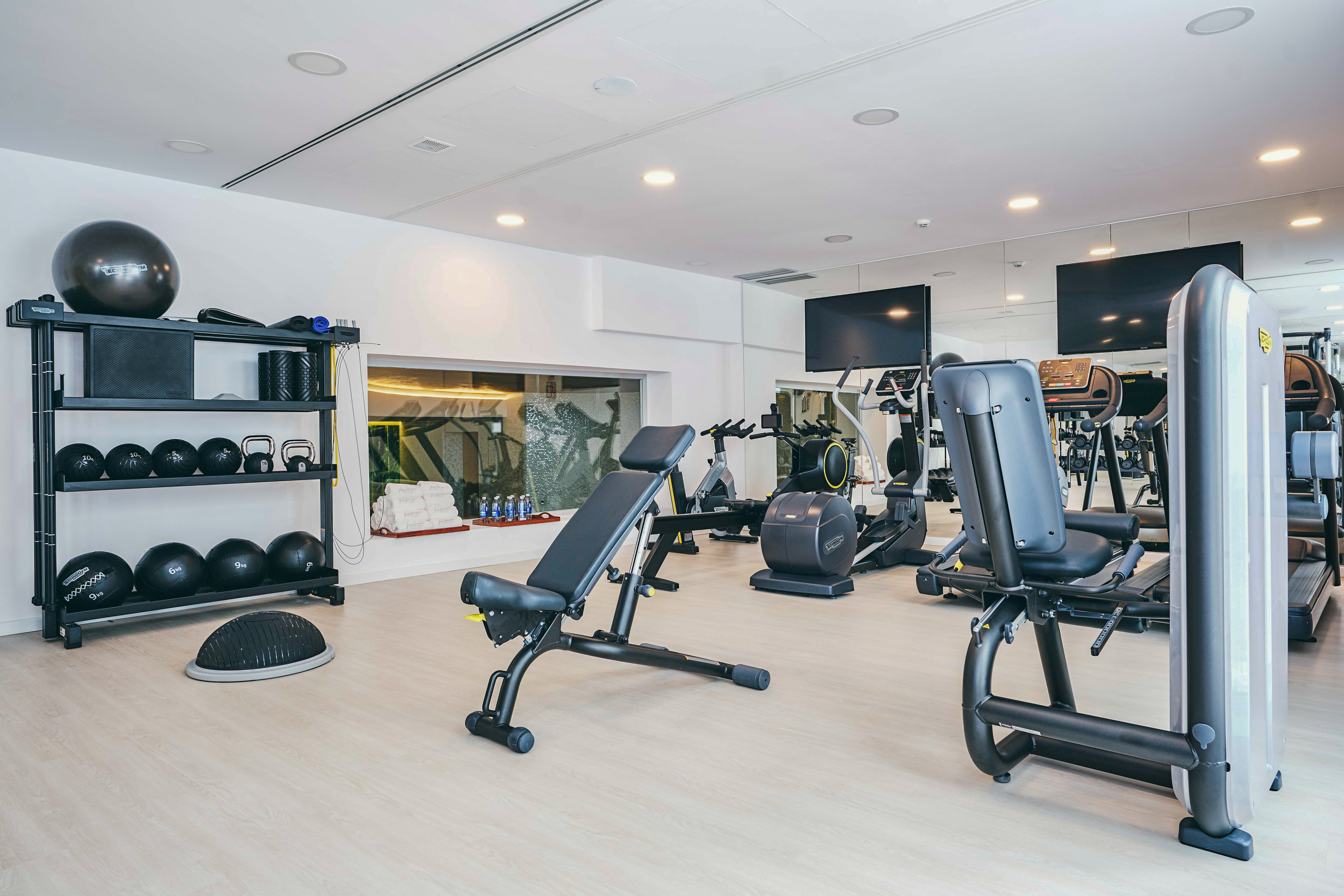 Modern gym with cardio machines, adjustable bench, and weight rack.