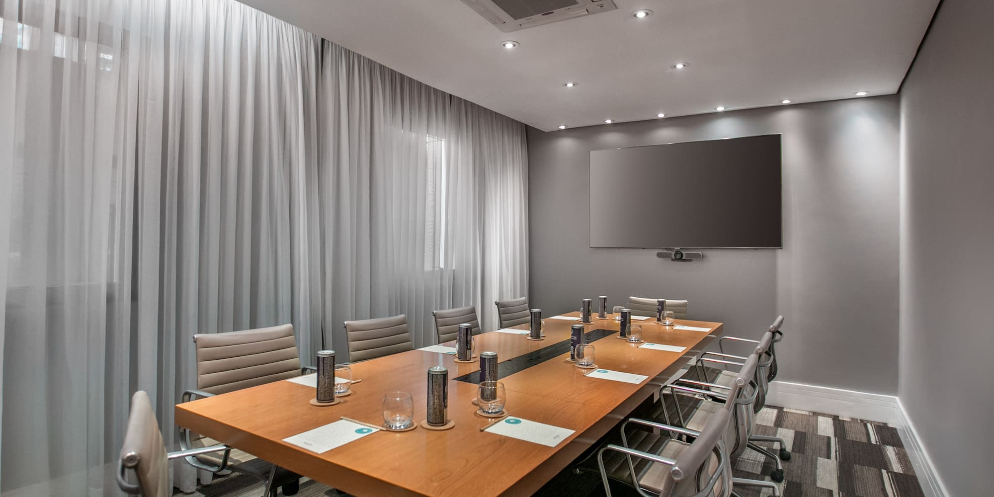Modern conference room with long wooden table, chairs, and large TV screen.