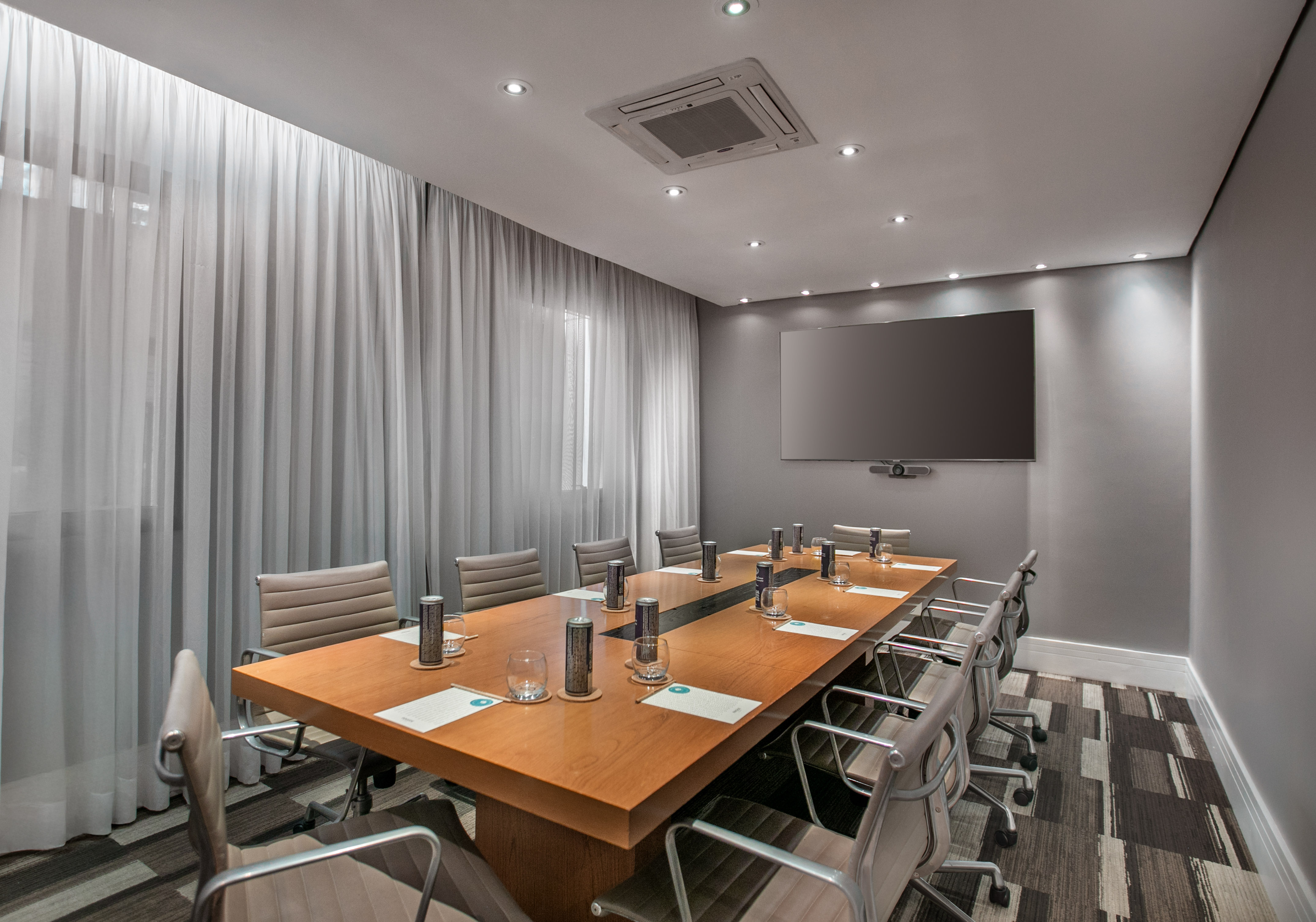 Modern conference room with long wood table, gray chairs, large screen, and curtains.