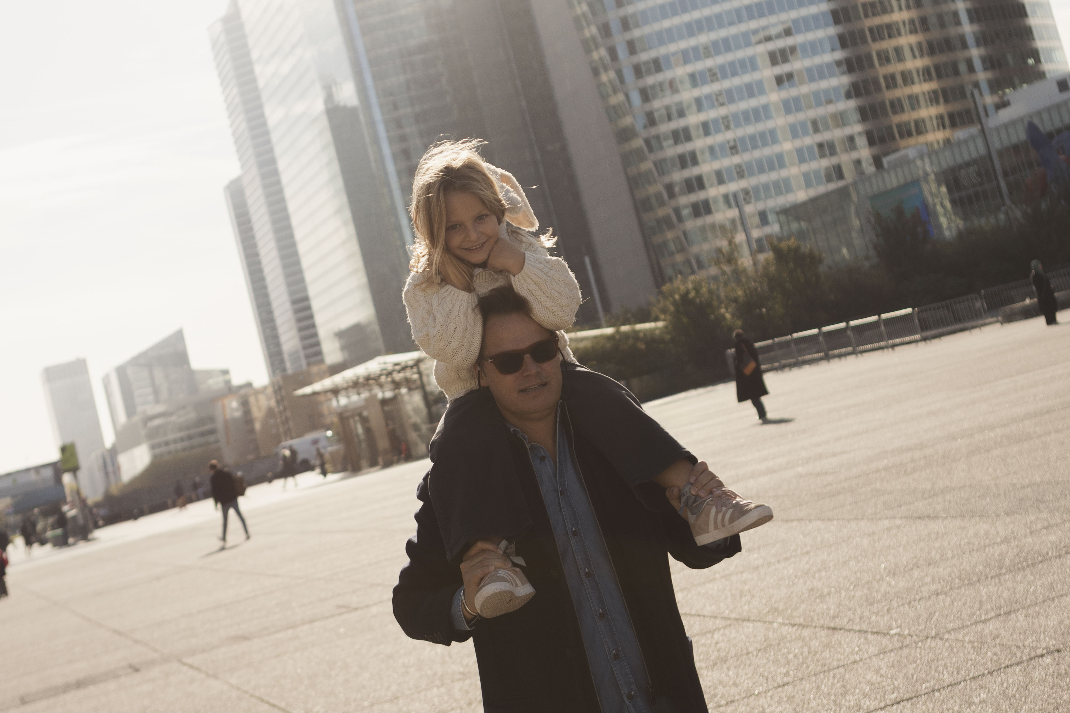 Smiling father giving daughter piggyback ride in sunny city with skyscrapers.
