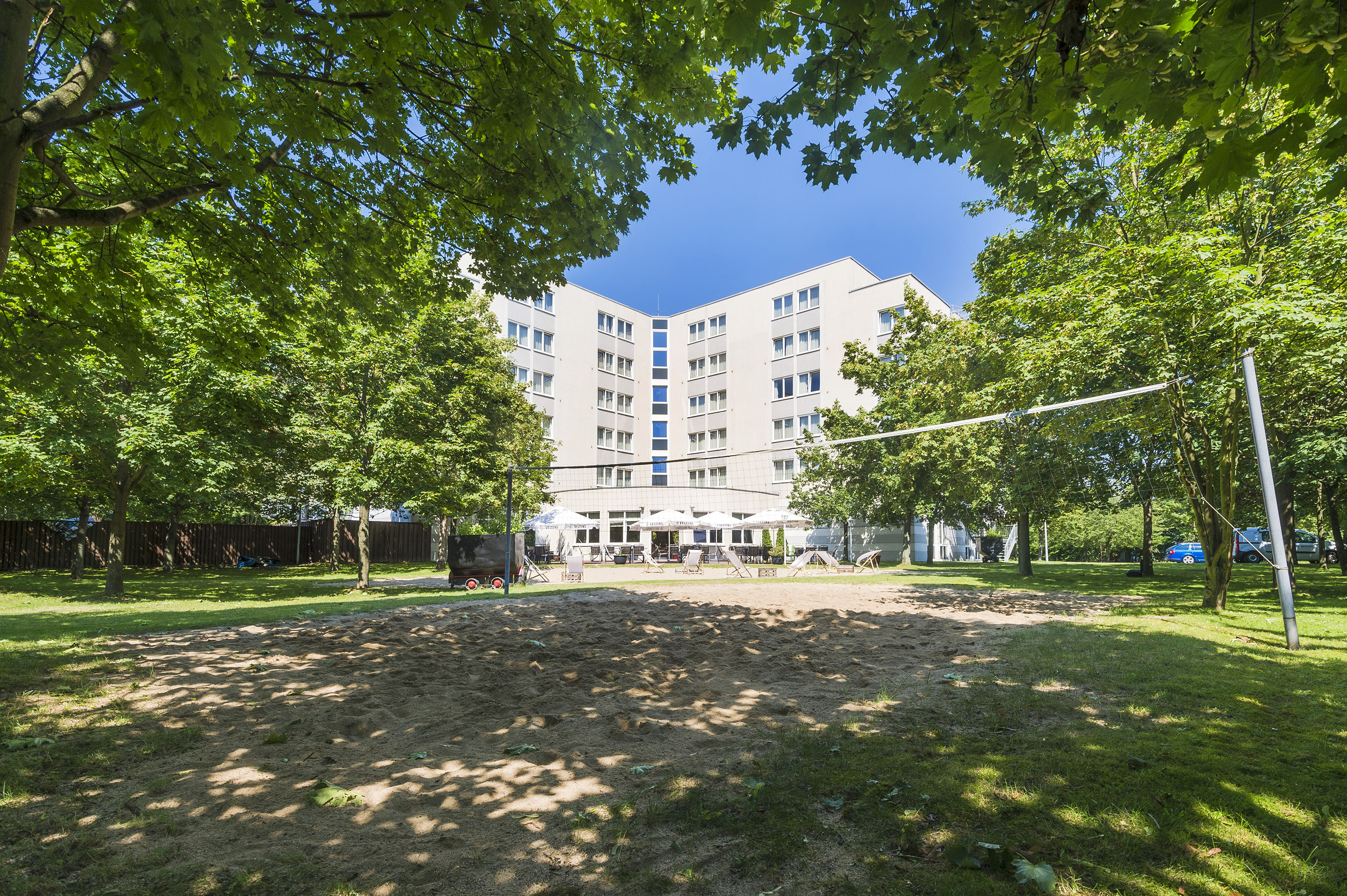 Beach volleyball court with hotel building and lush green trees on a sunny day.
