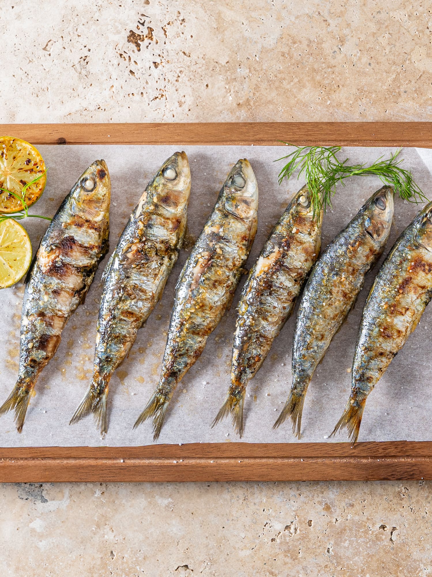 Sardinas a la parrilla con limón y eneldo en tabla de madera.