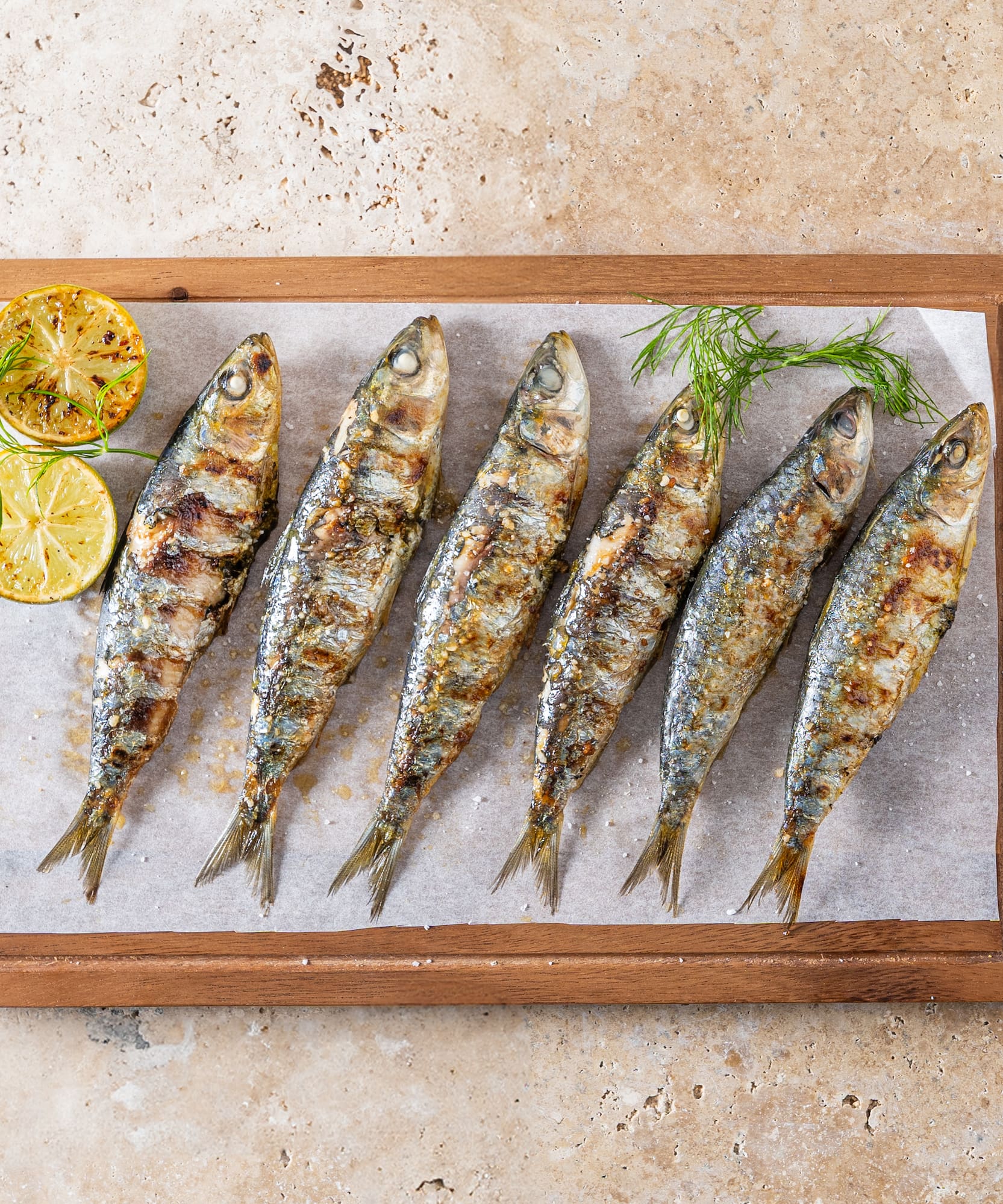 Sardinas a la parrilla con limón y eneldo en tabla de madera.