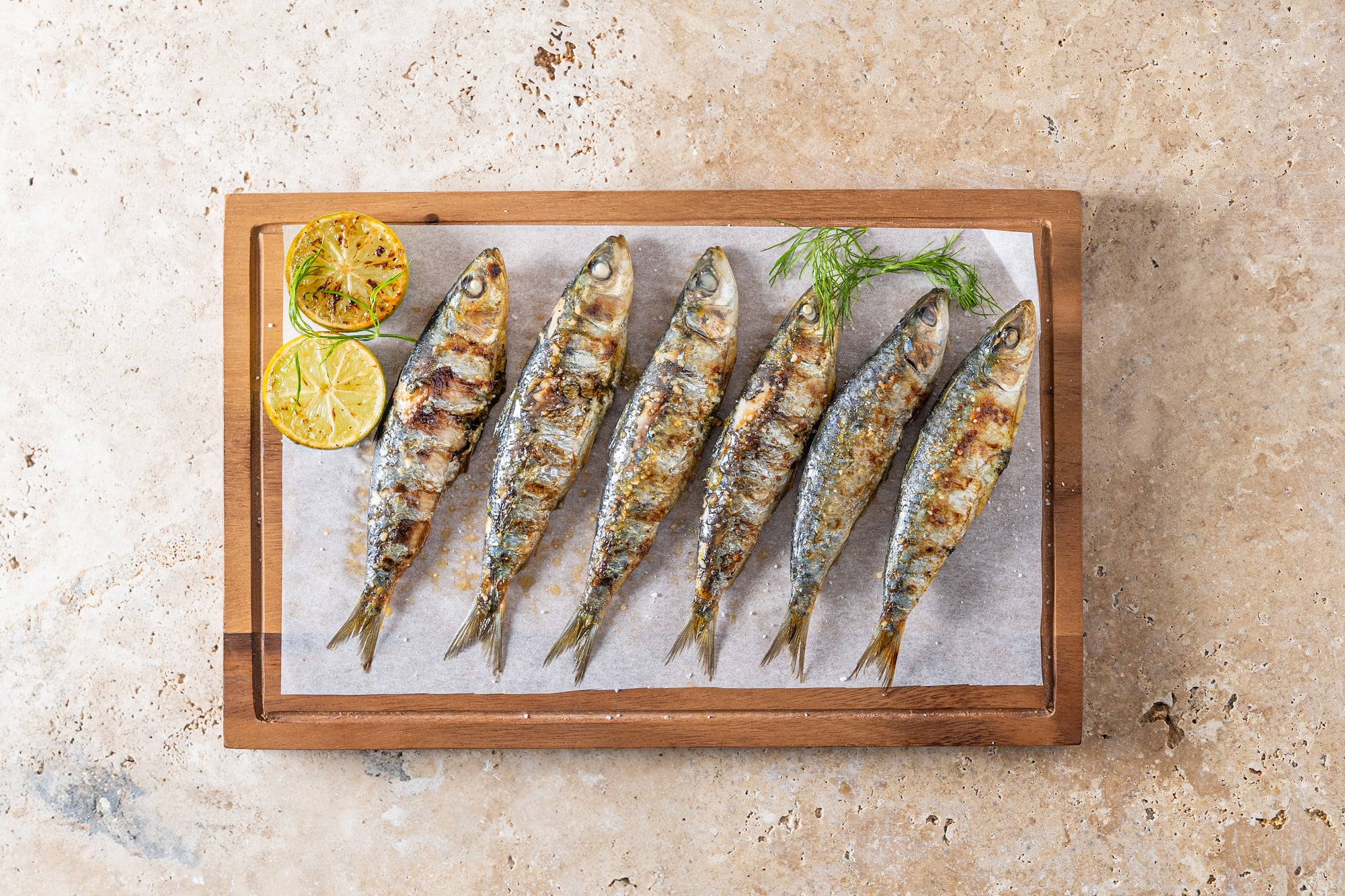 Sardinas a la parrilla con limón y eneldo en tabla de madera.