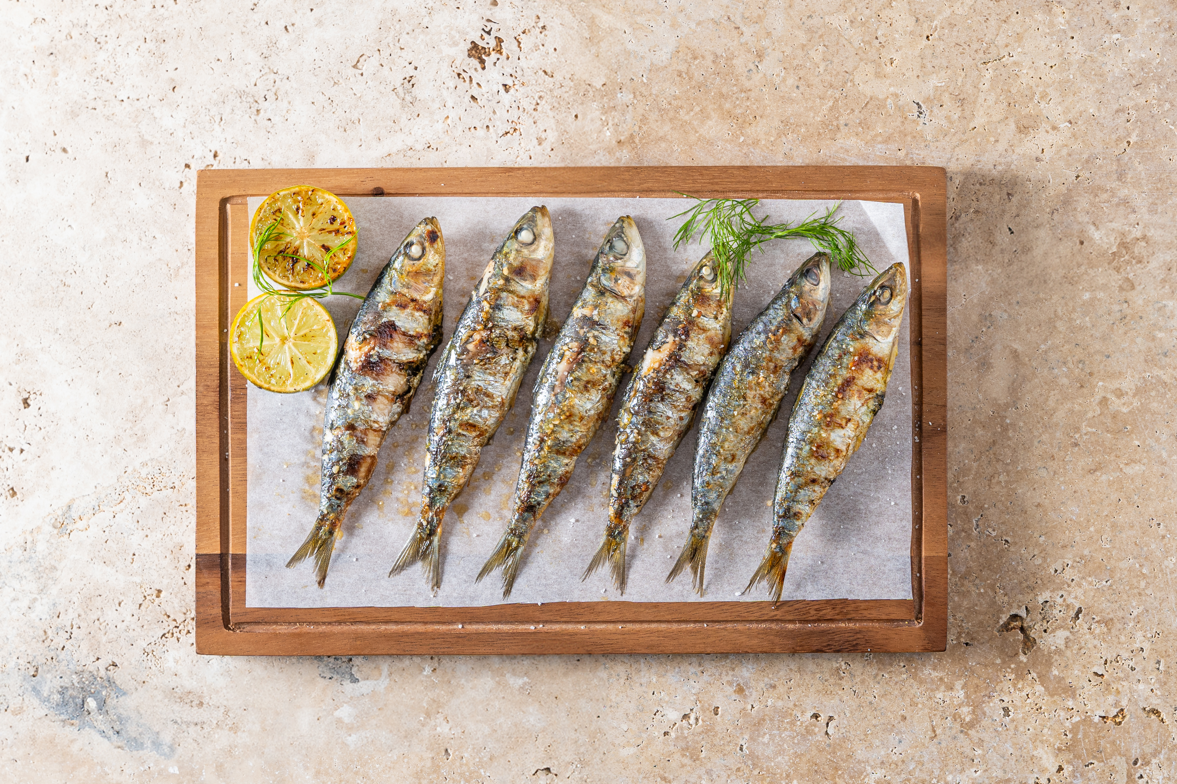 Sardinas a la parrilla con limón y eneldo en tabla de madera.