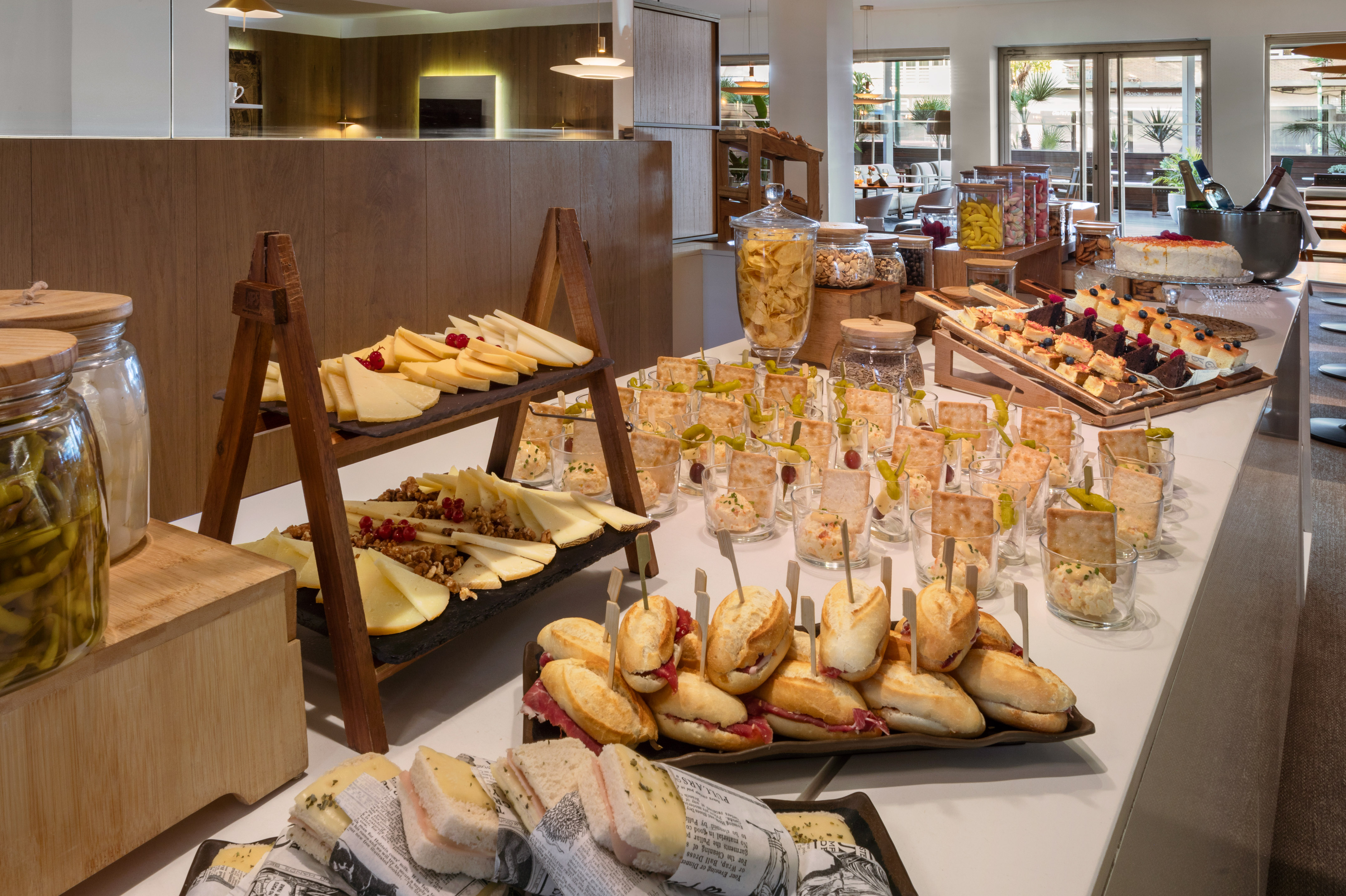 Diverse buffet display: cheese board, mini sandwiches, individual appetizers, pastries.