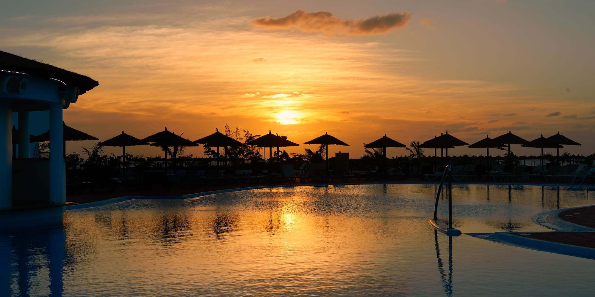 a pool with umbrellas and a sunset
