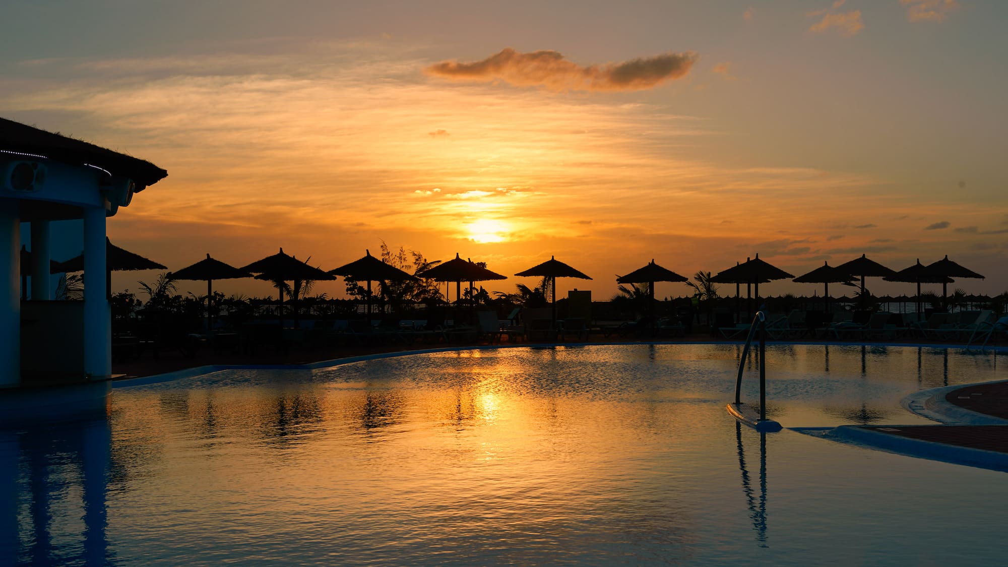 a pool with umbrellas and a sunset