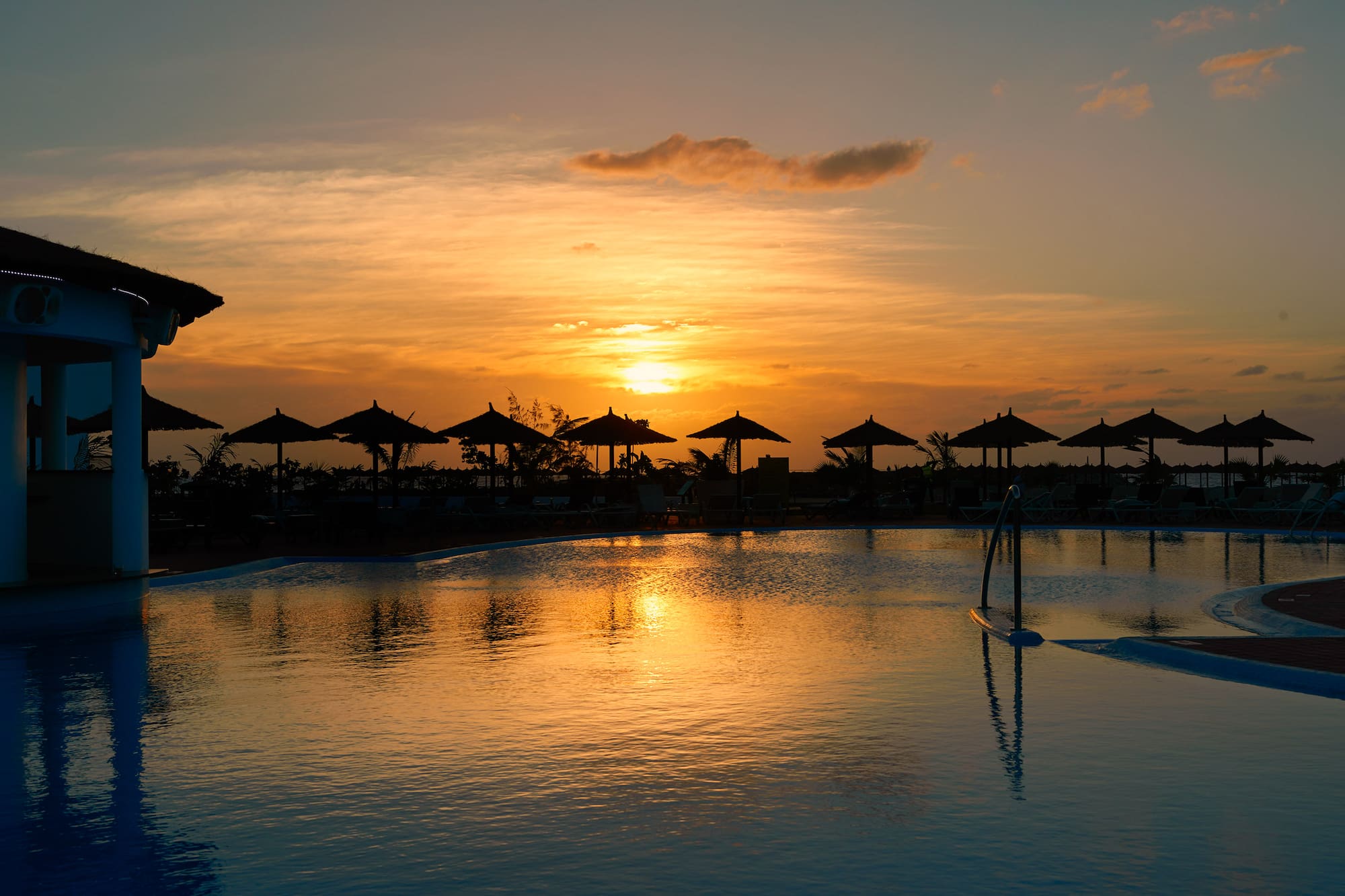 a pool with umbrellas and a sunset